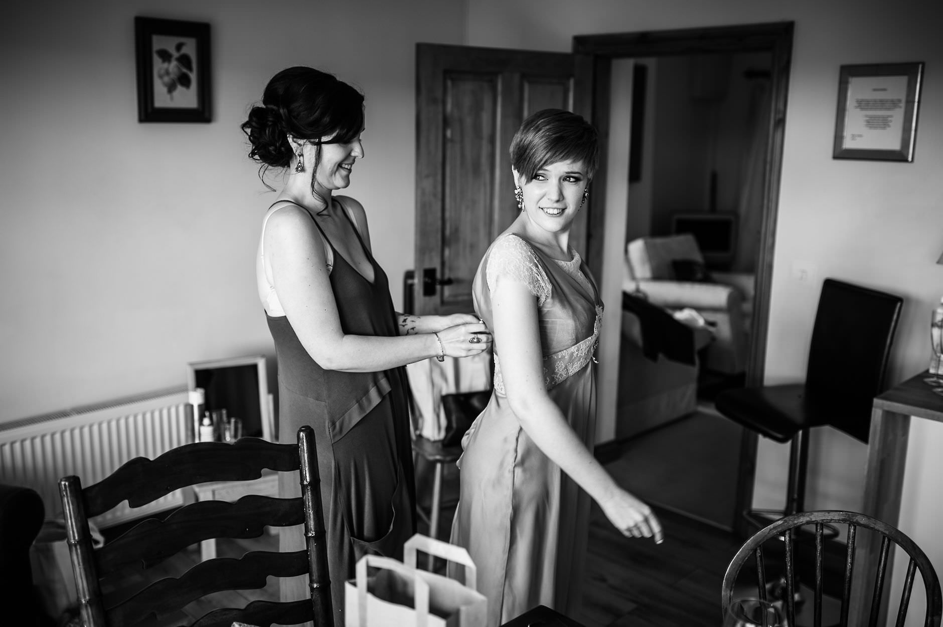 bride helps bridesmaid with her dress