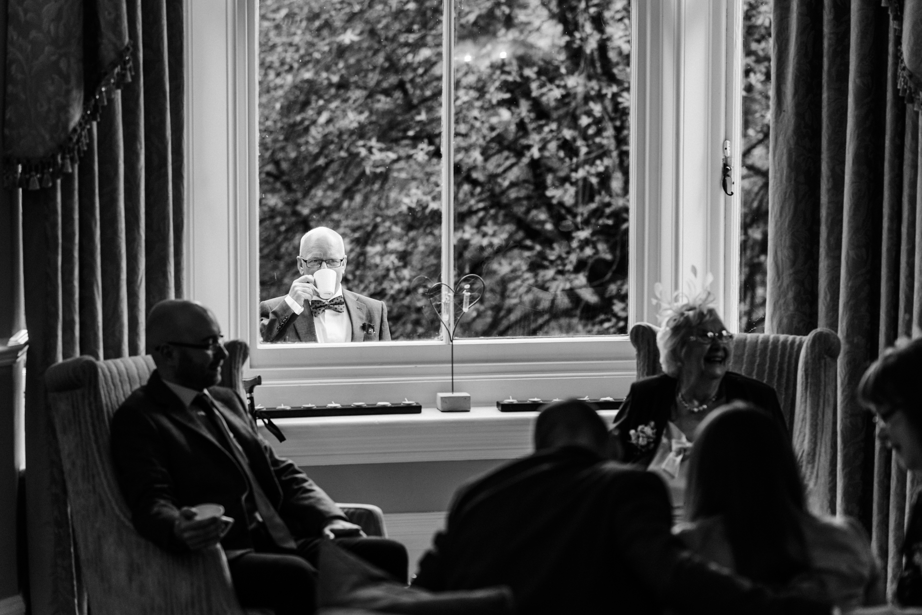man drinking a cup of tea at the window looking in