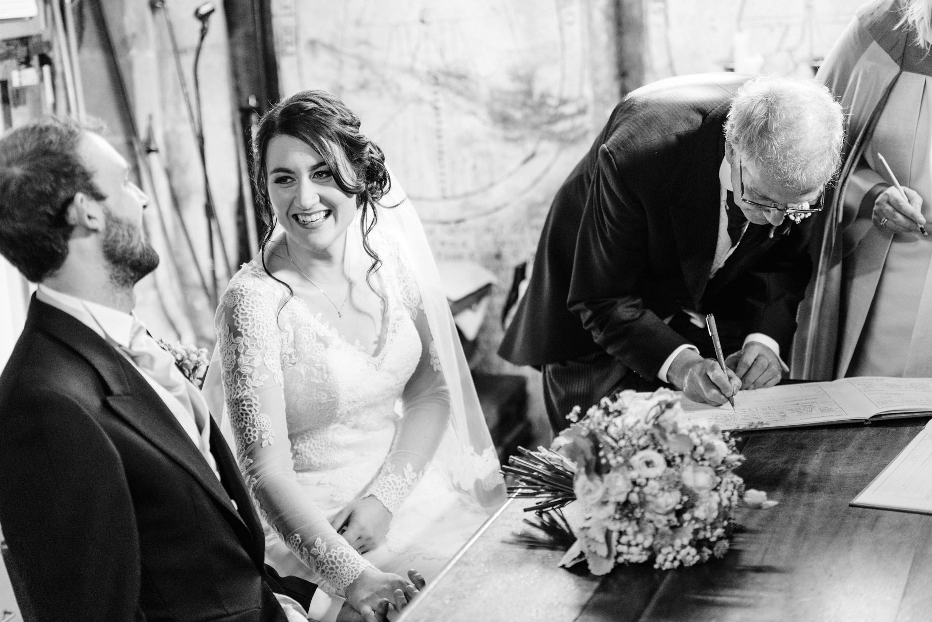 Bride smiling at her husband as witness signs the register