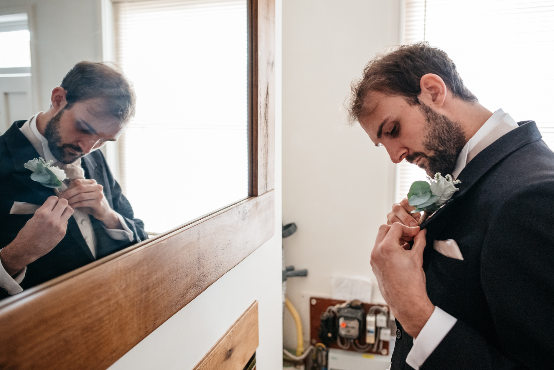 Groom stood in front of a mirror fixing his button hole