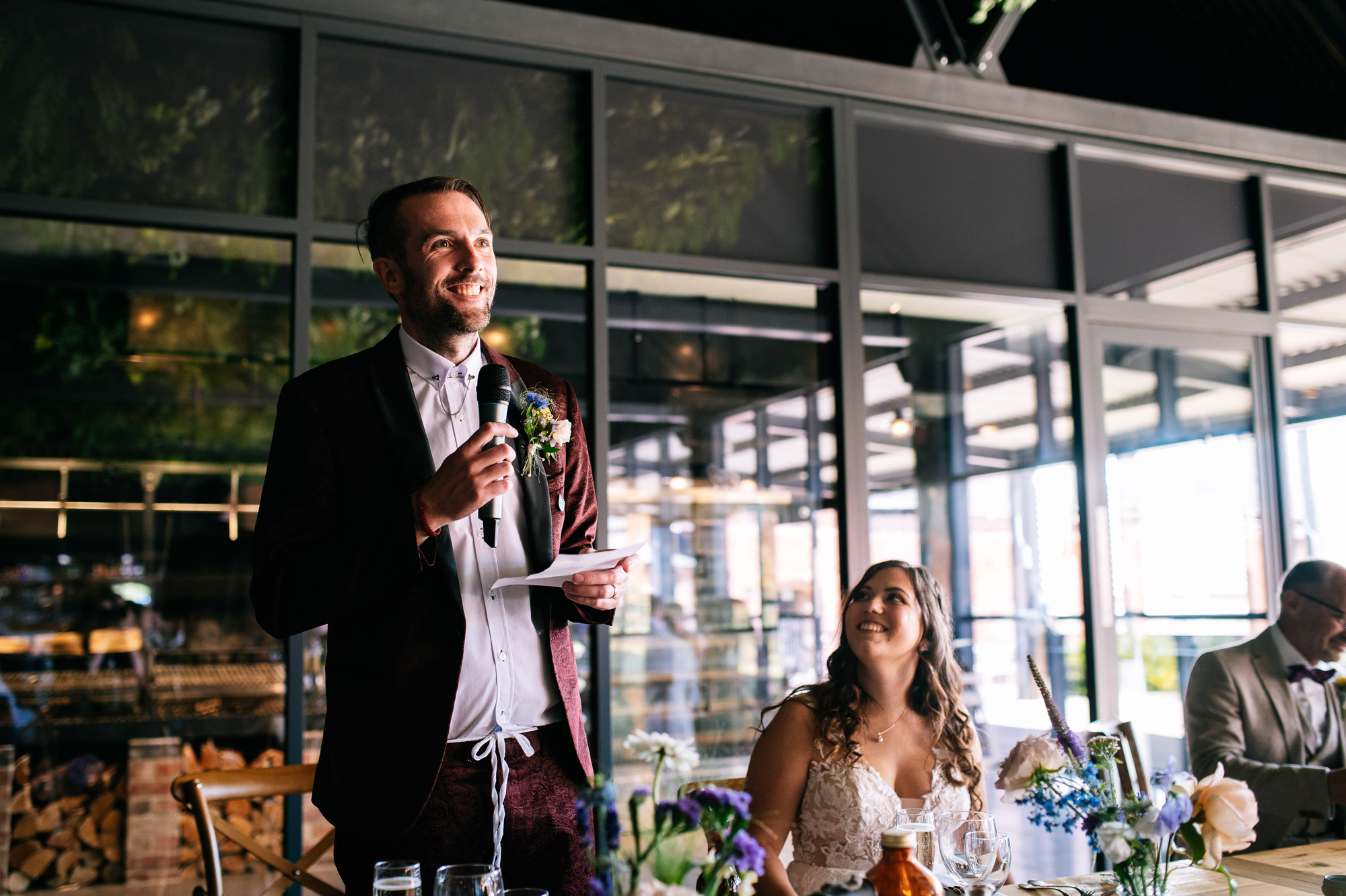 smiling groom giving a speech while the bride watches