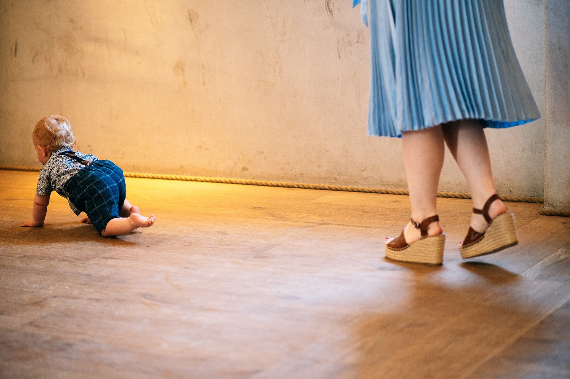 baby crawling on the floor with his mum's feet following behind him