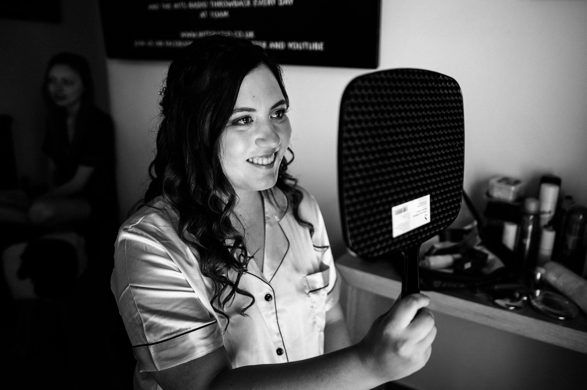smiling bride holding a hand mirror looking at her makeup