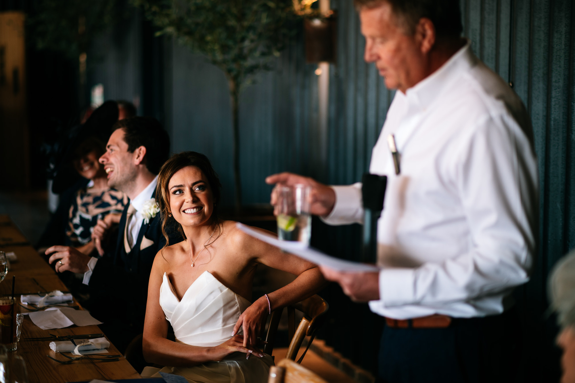 bride smiling at her dad as he gives his speech