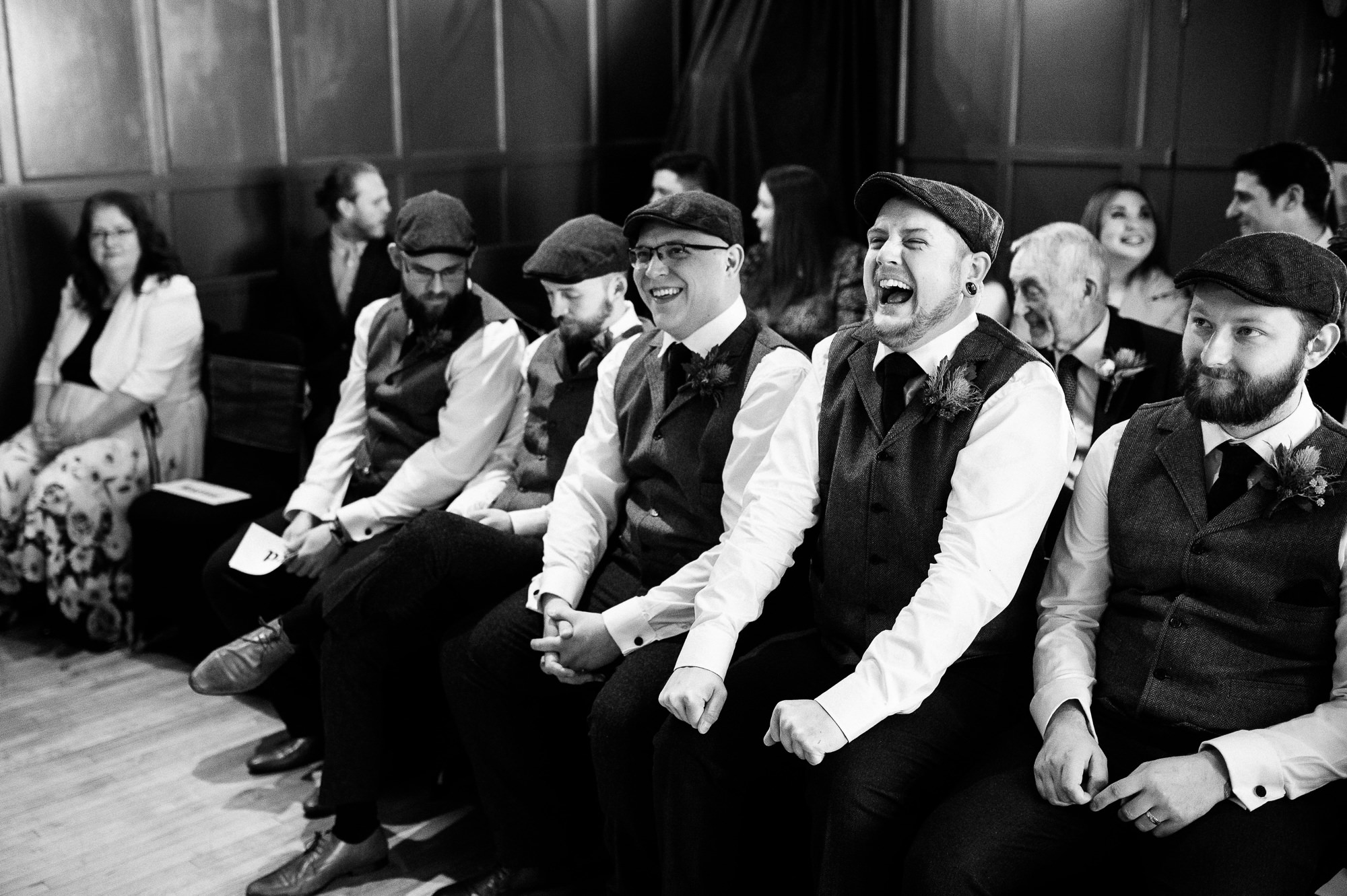 groomsmen sat in a row laughing during the ceremony