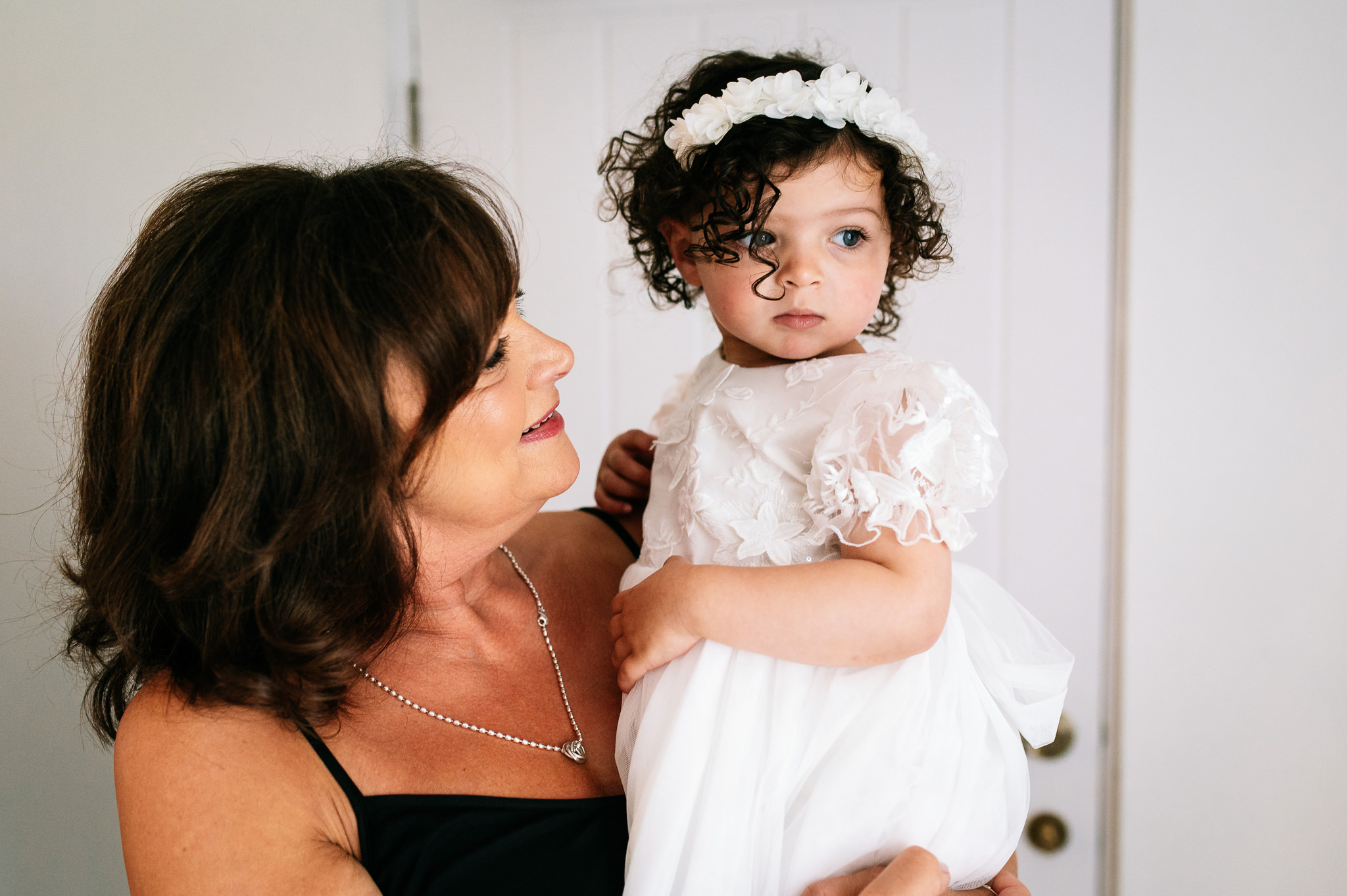 mother of the bride holding her young granddaughter who's wearing a white dress and headband