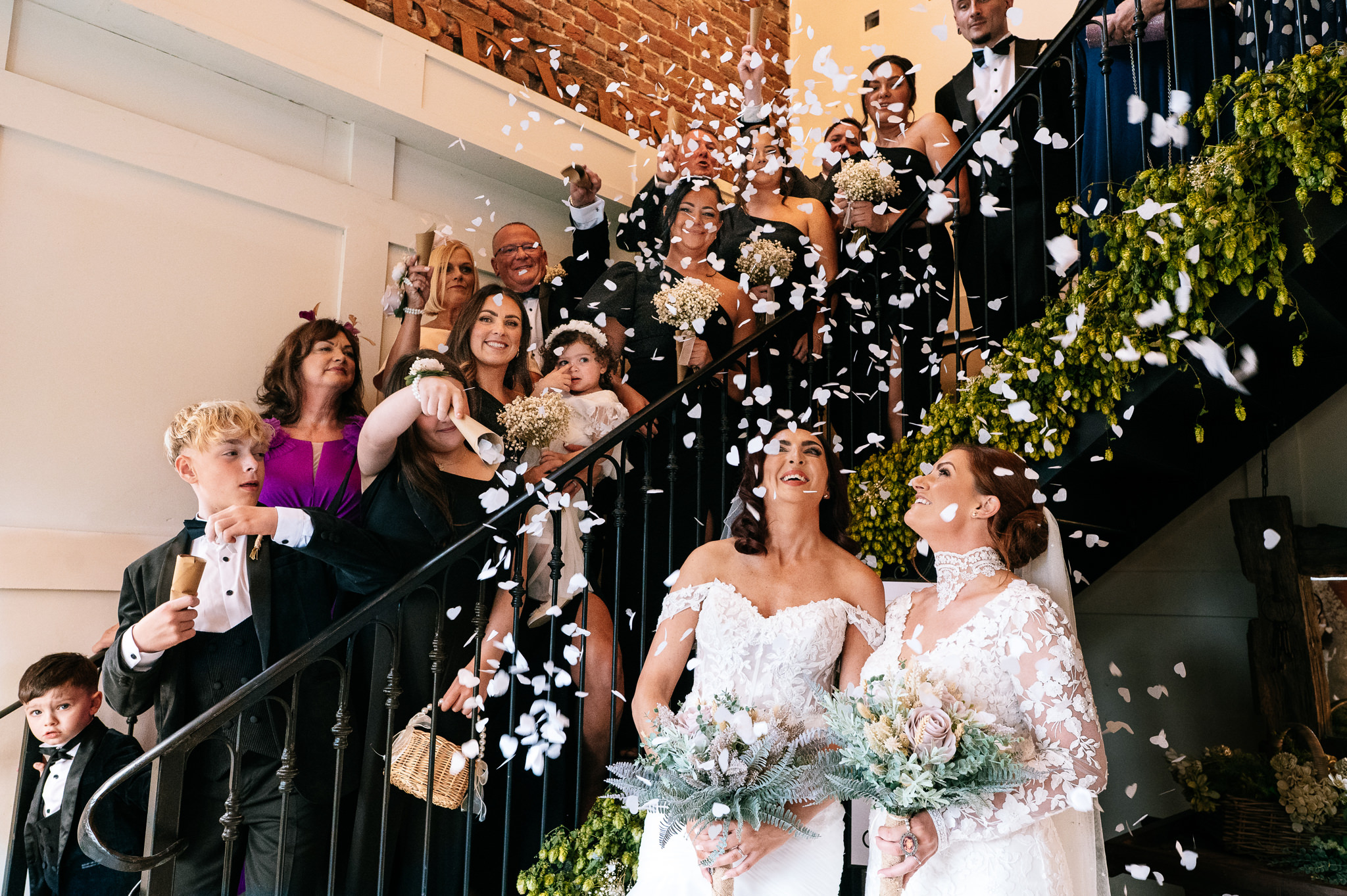 brides looking up as their guests throw confetti down from an iron staircase