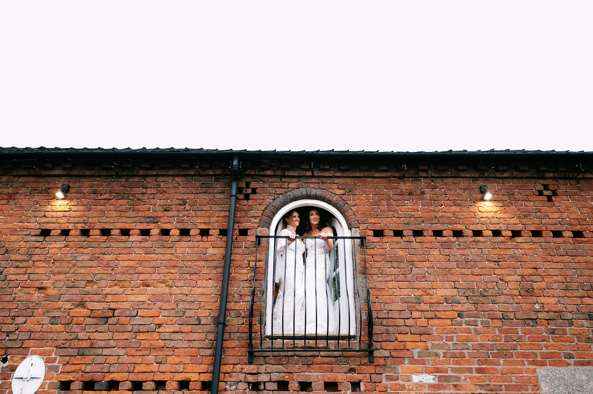 two brides stood at the juliet balcony in the ceremony barn at the cheshire venue