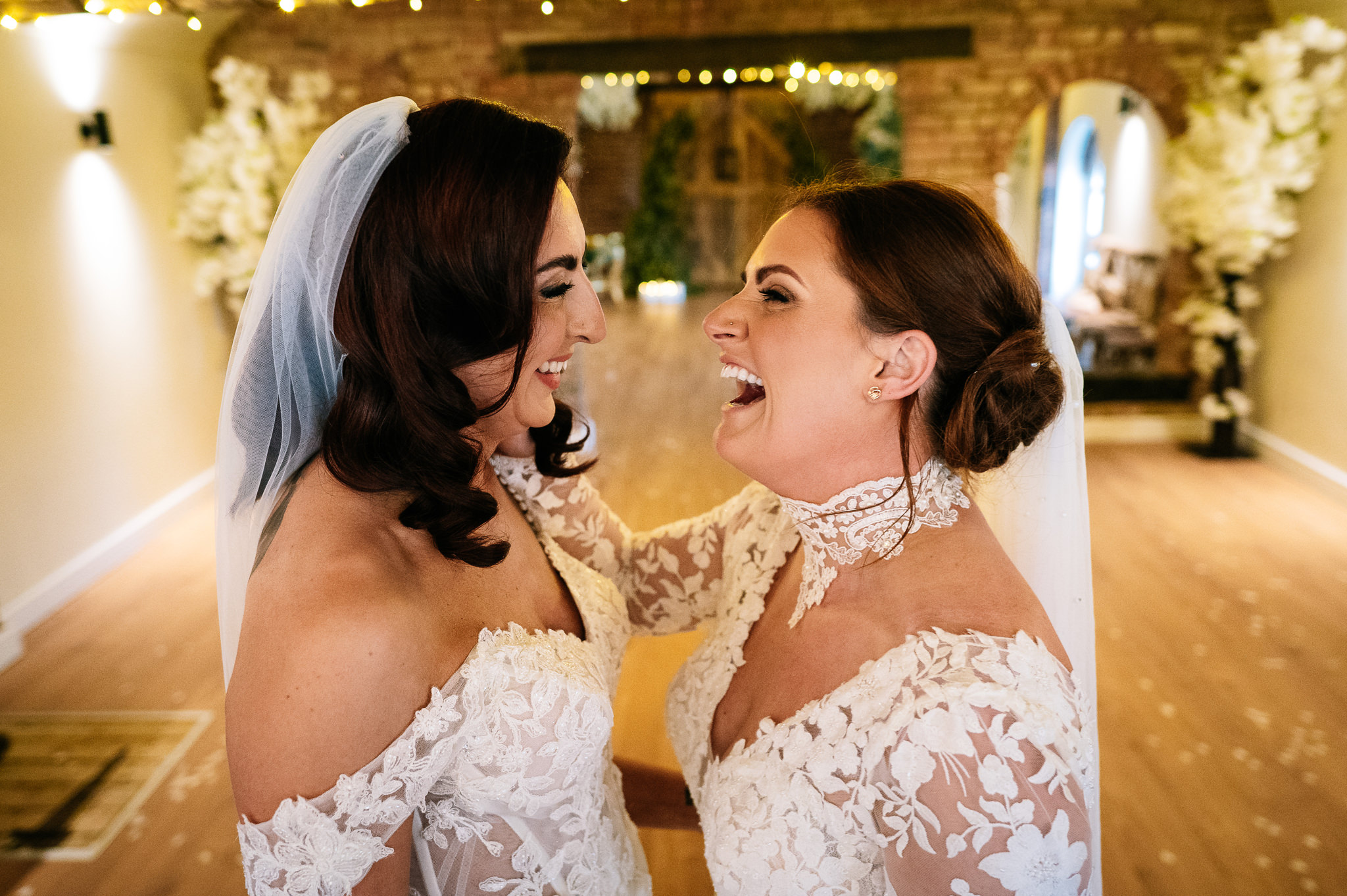 two brides facing each other and laughing in the barn at The Cheshire Venue