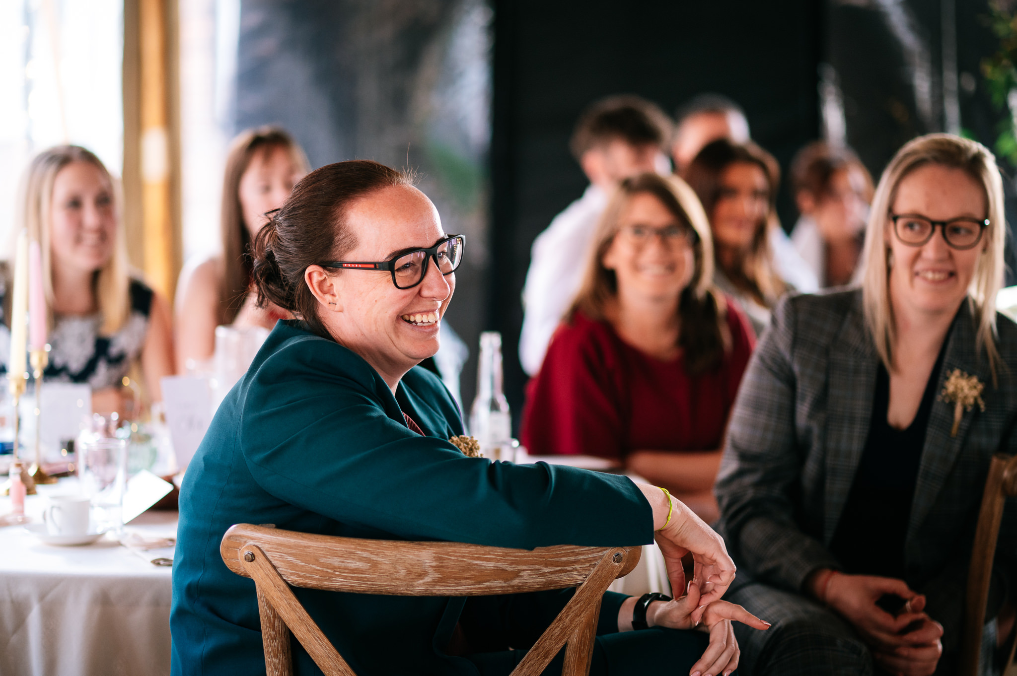 a woman wearing a green jacket and glasses laughing during the speeches