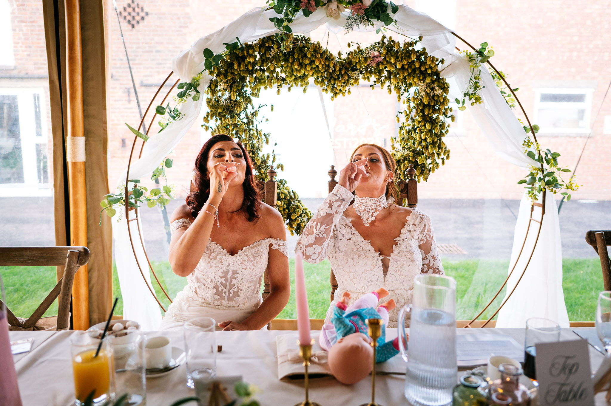 two brides sat at the top table drinking a shot