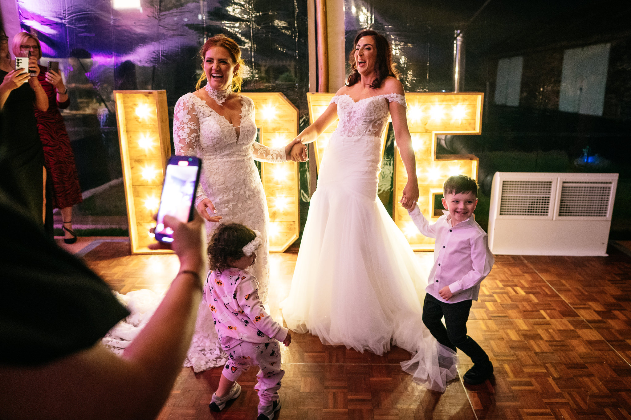 two brides laughing and enjoying their first dance with their two young children