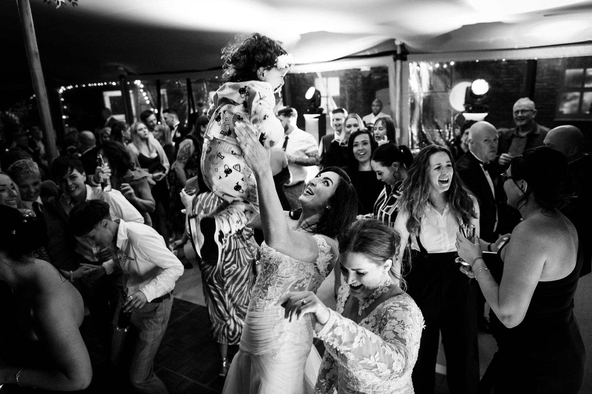 a bride on the dancefloor smiling and playfully throwing her toddler in the air