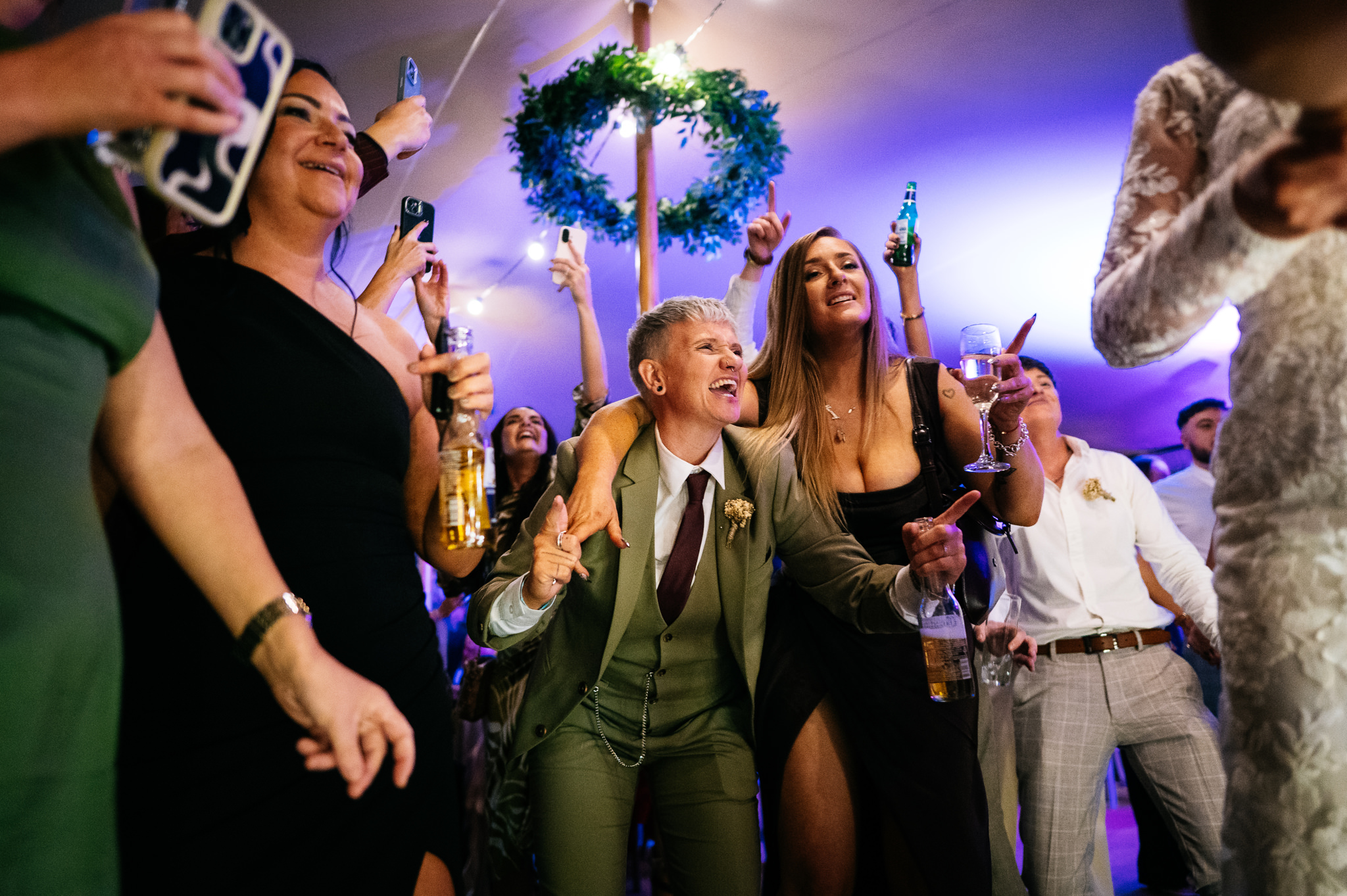 wedding guests on the dancefloor holding drinks singing and pointing their fingers