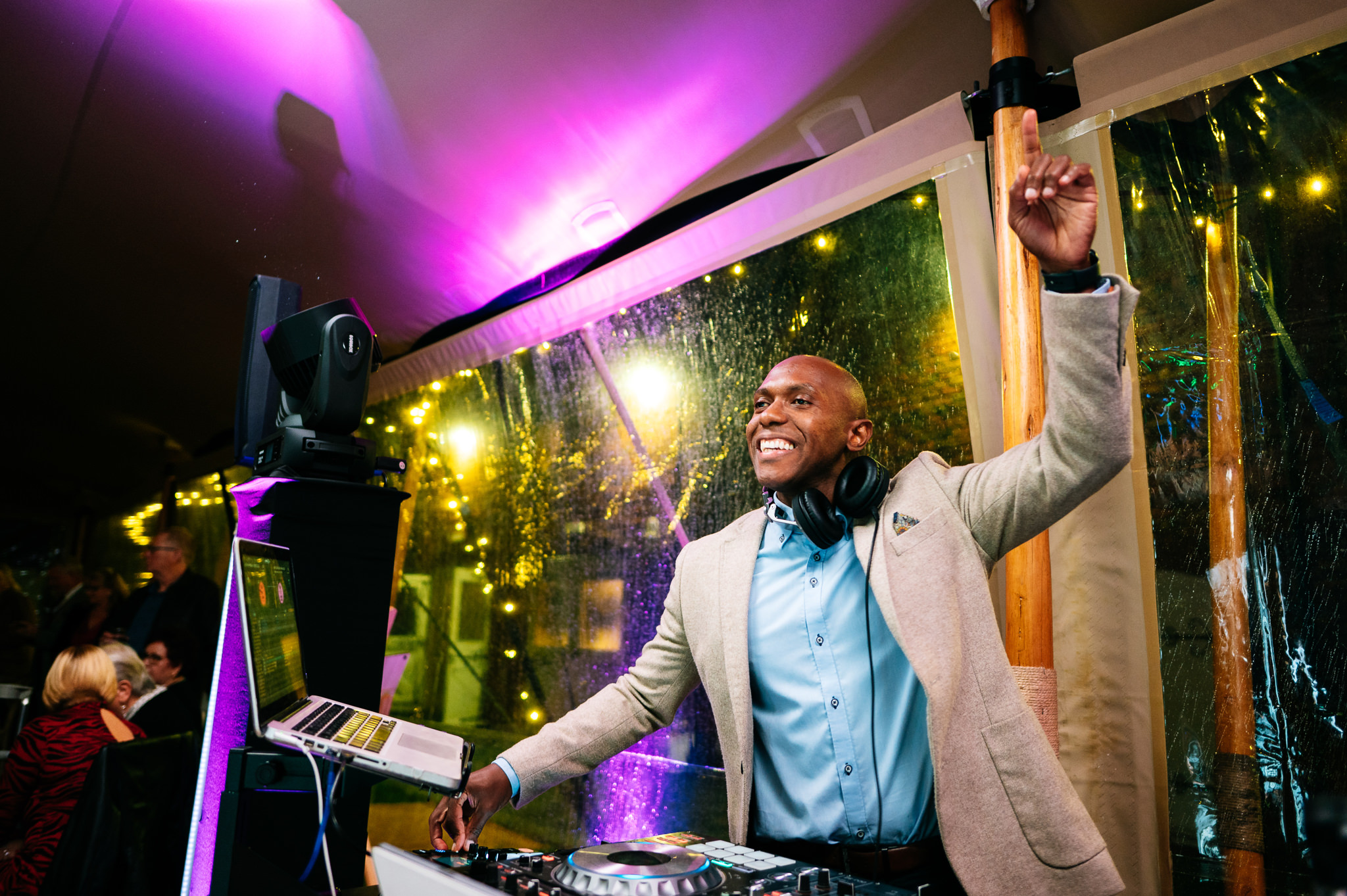 a happy wedding dj wearing a suit jacket and blue shirt with his hand in the air