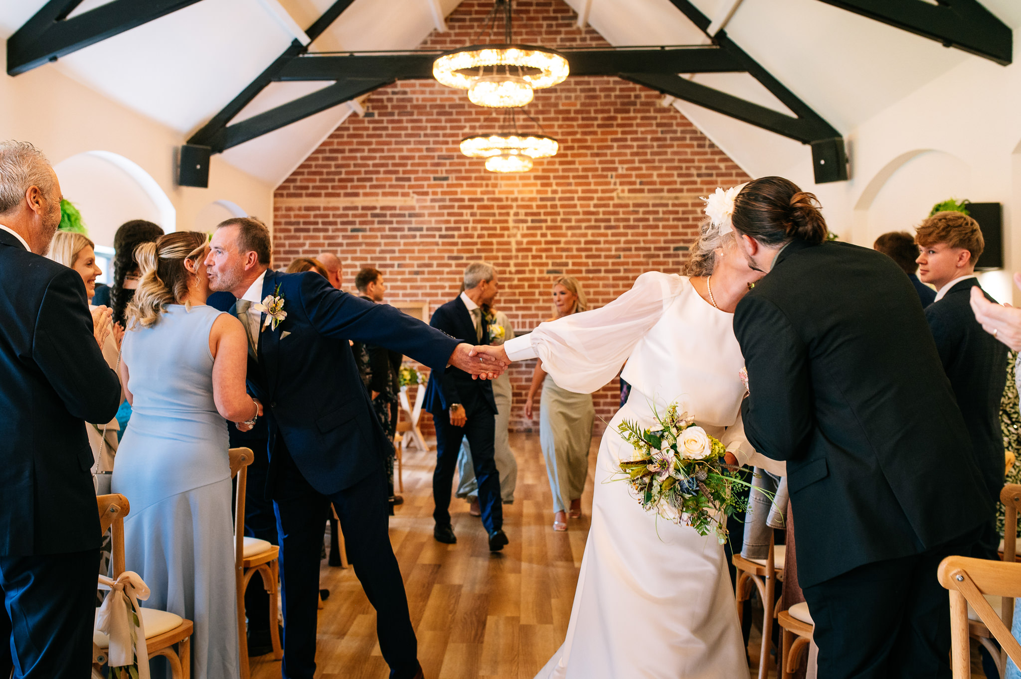 just married couple walk down the aisle together kissing guests on either side of the aisle whilst still holding hands