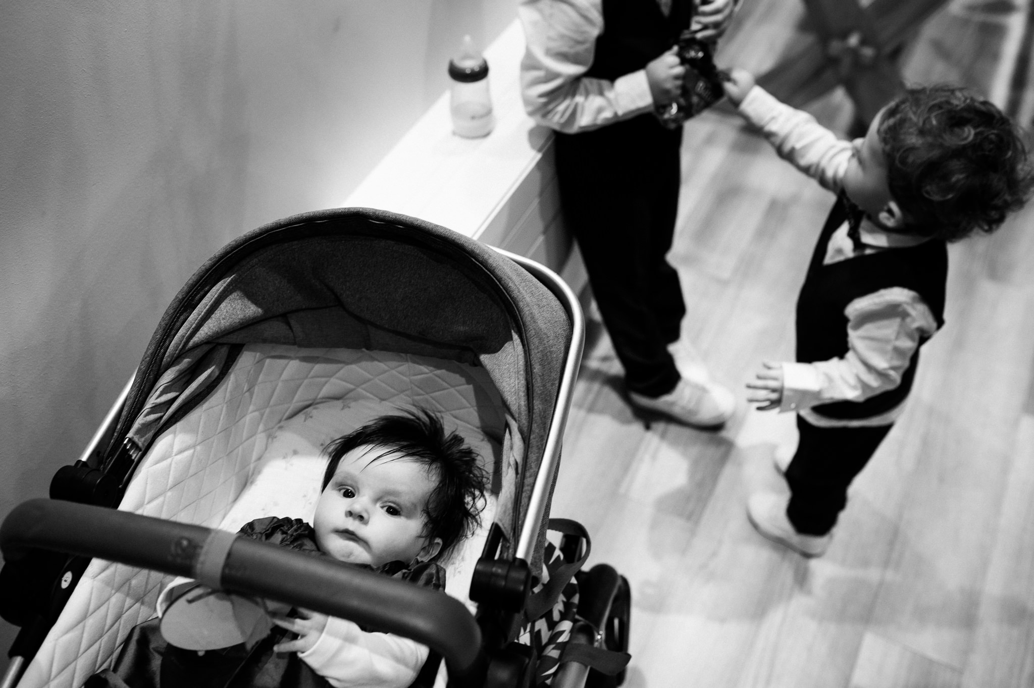 young baby resting in her pram while her brothers play behind her