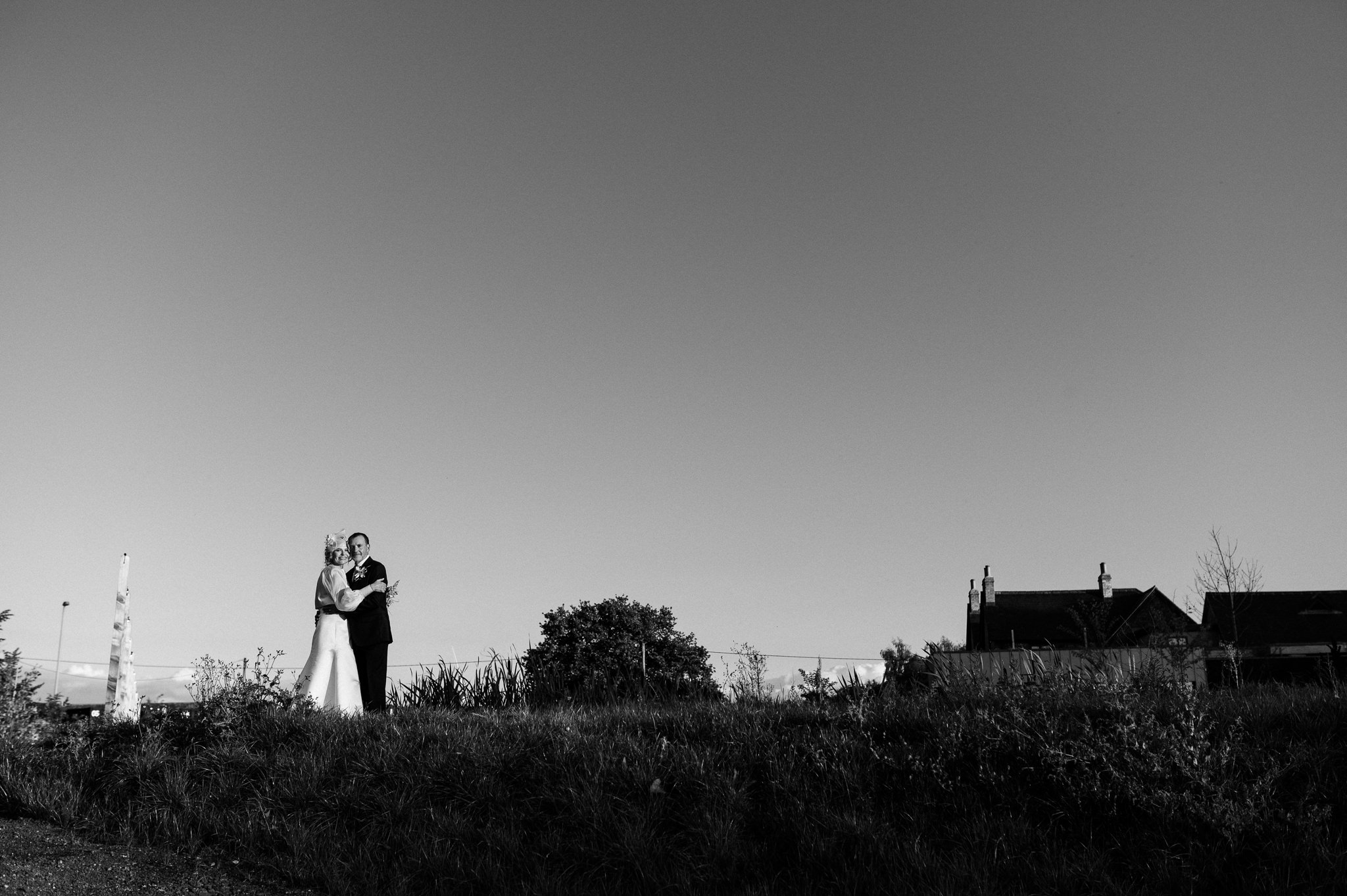 a black and white photo of a bride and groom embracing with a big sky behind them
