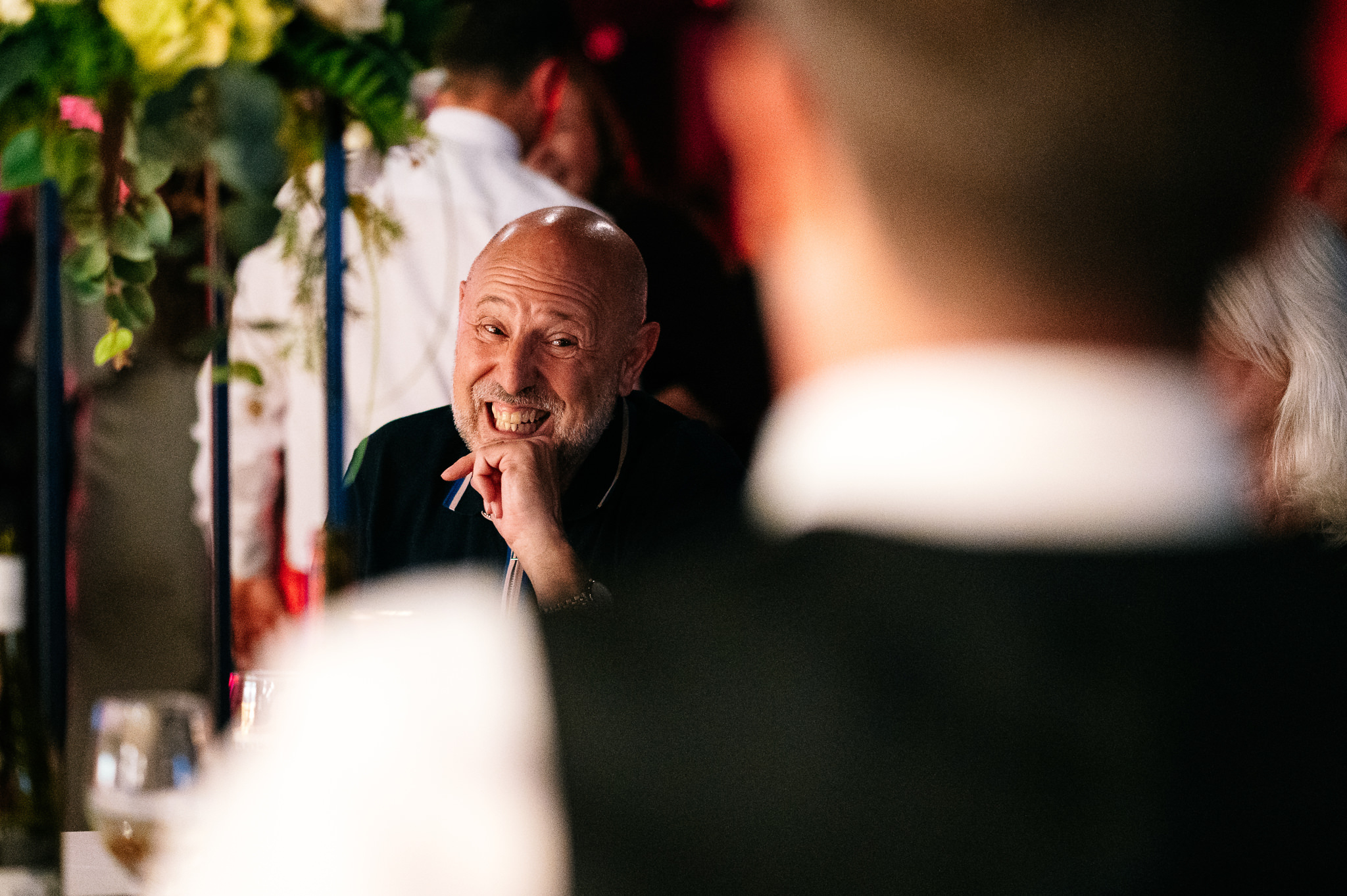 An older man with short hair and a white beard smiling at a friend across the table