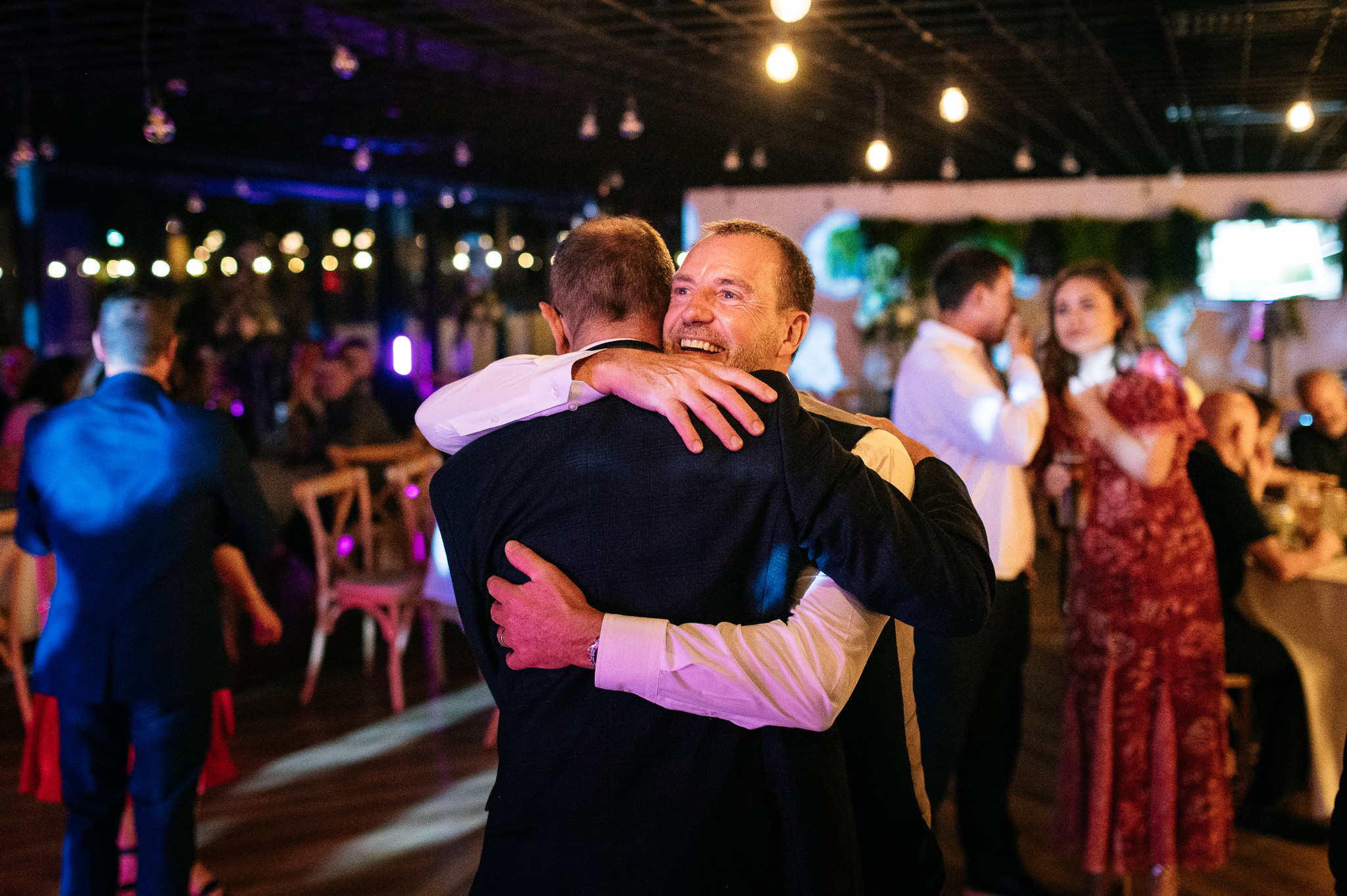a happy groom hugging a friend on the dancefloor