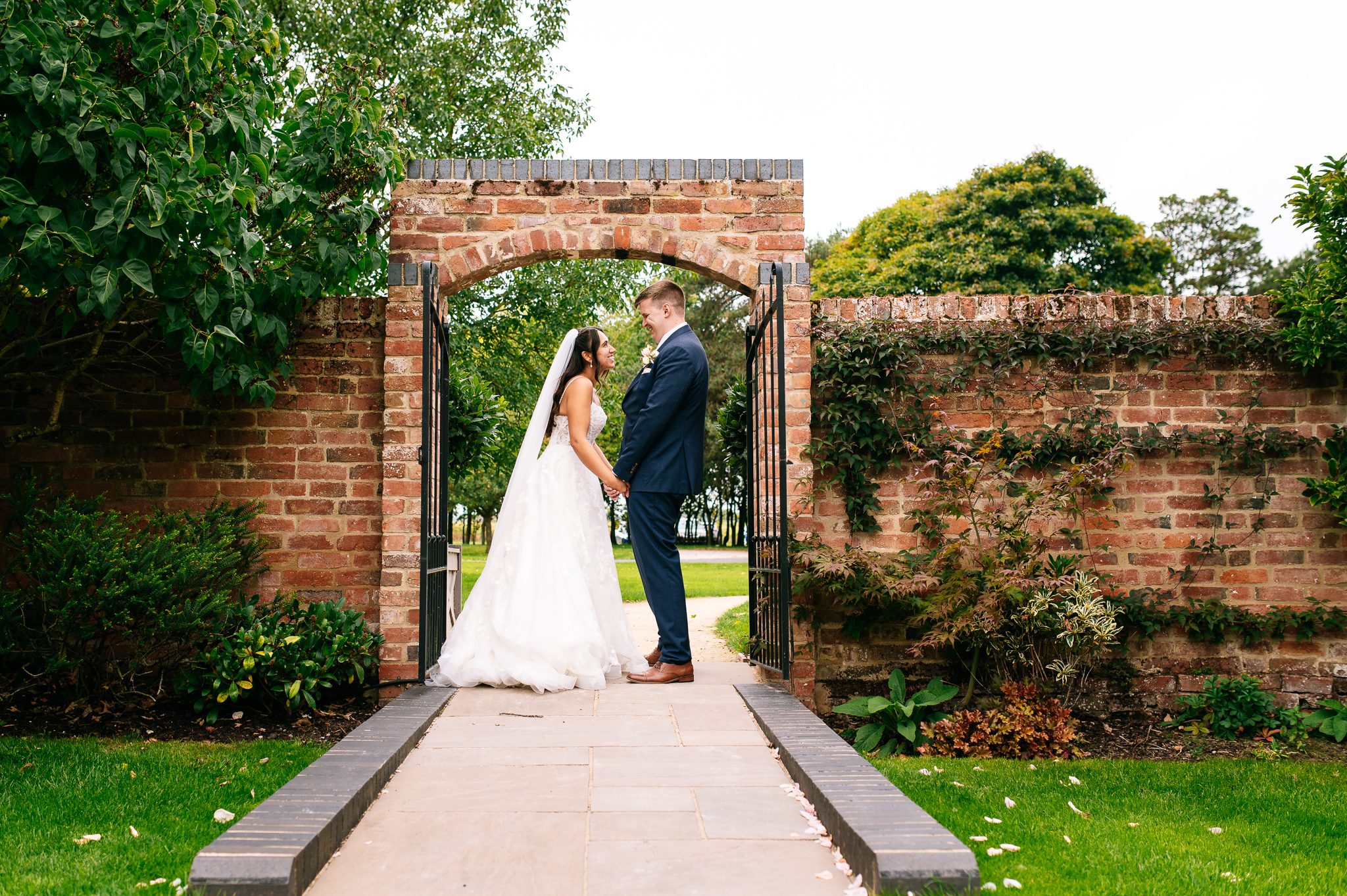 bride and groom stood holding hands and laughing under an archway in a walled garden