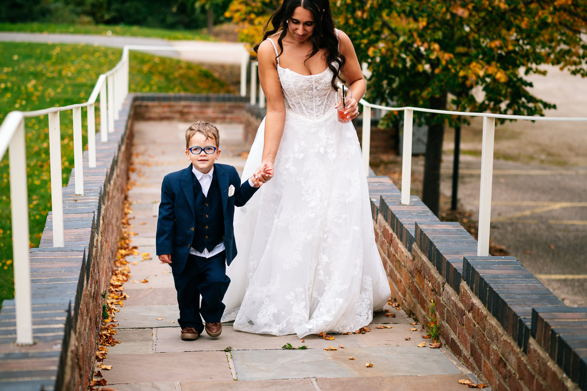 young page boy in a 3 piece suit holding hands with the bride as they walk along a path outside