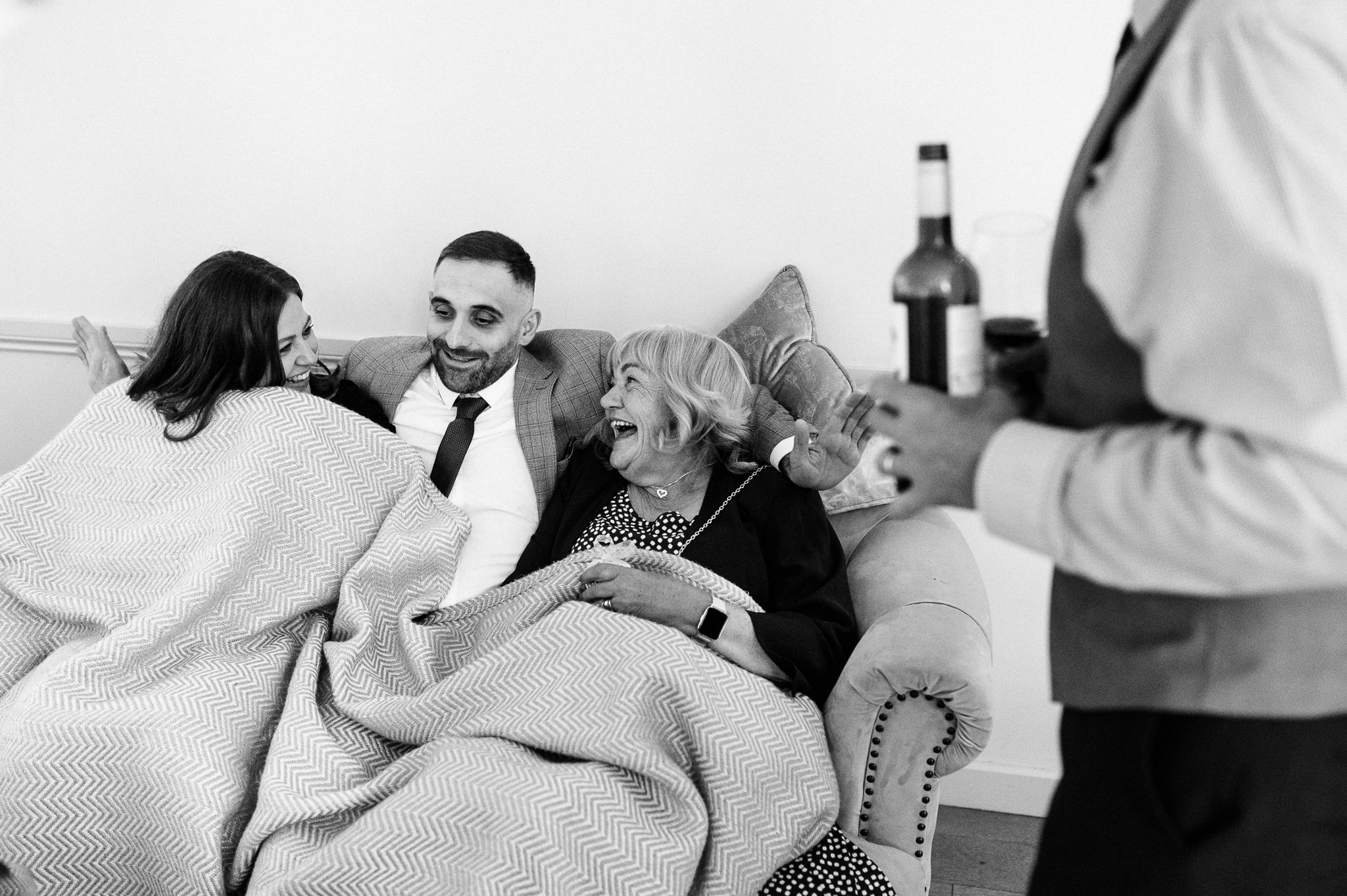 funny black and white photo of a male wedding guest under a blanket with two women