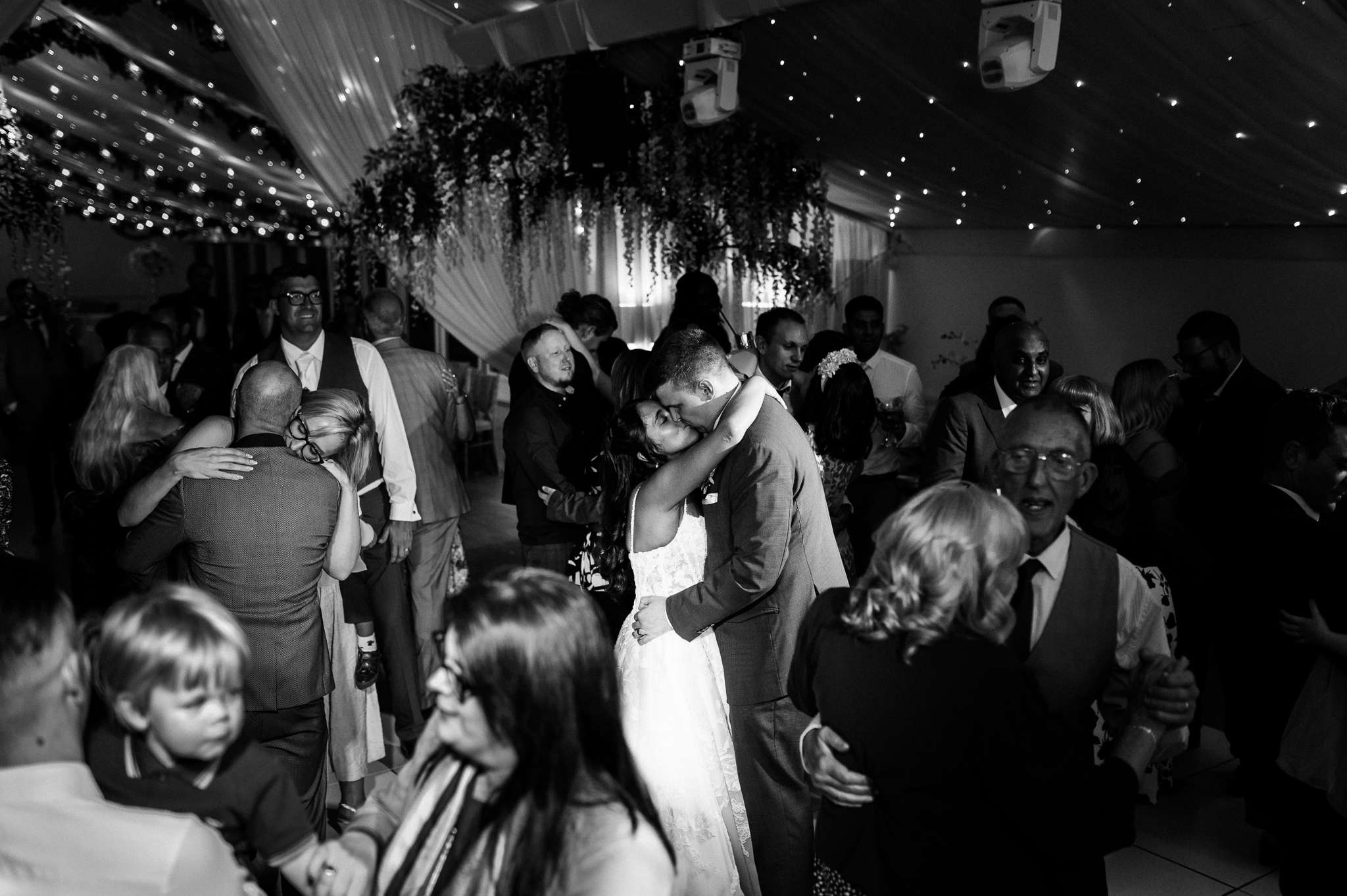 black and white photo of a couple kissing in the middle of a busy dance floor at alrewas hayes wedding venue