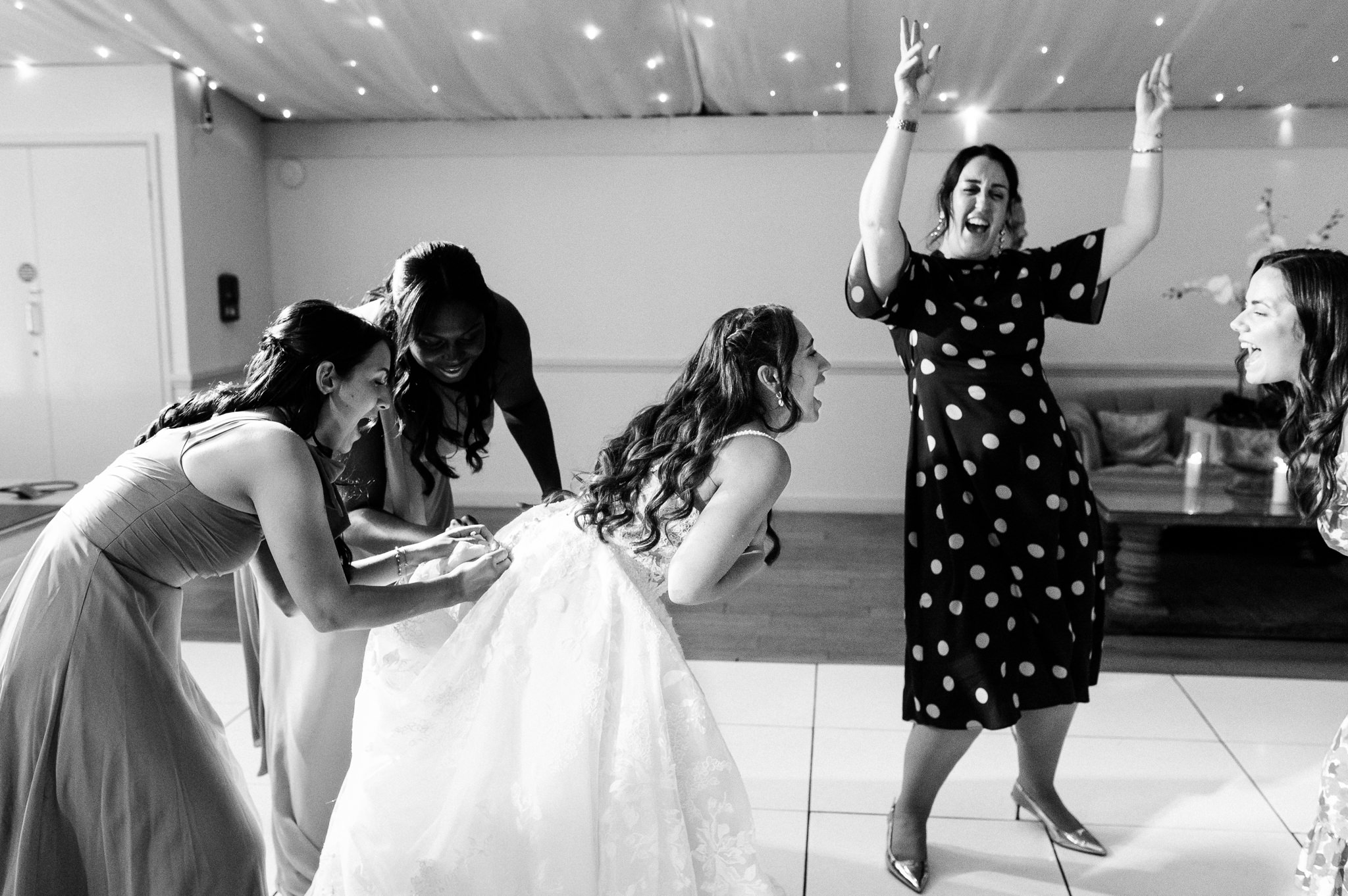 black and white photo of the bride having her dress buttoned up on the dance floor