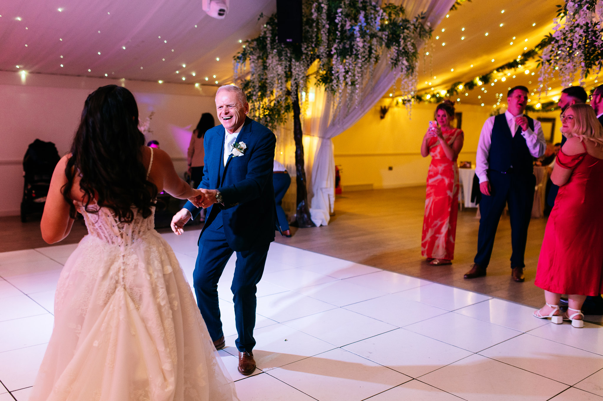 smiling man in a blue suit dancing with a bride on her wedding day