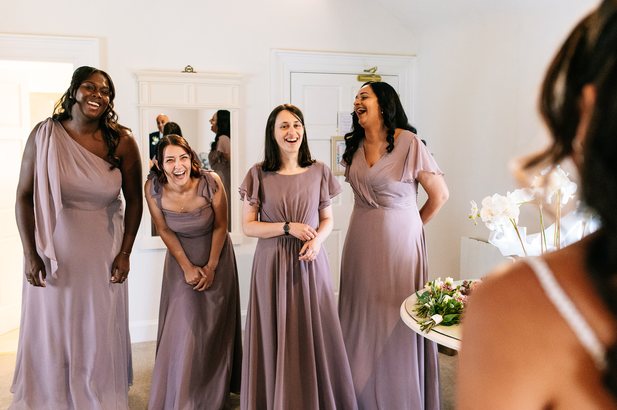 happy smiling bridesmaids react to seeing the bride in her dress