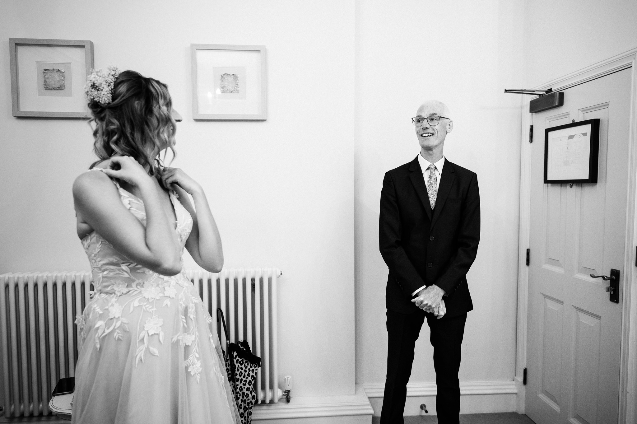 black and white photo of the father of the bride wearing a suit and smiling at his daughter in her wedding dress