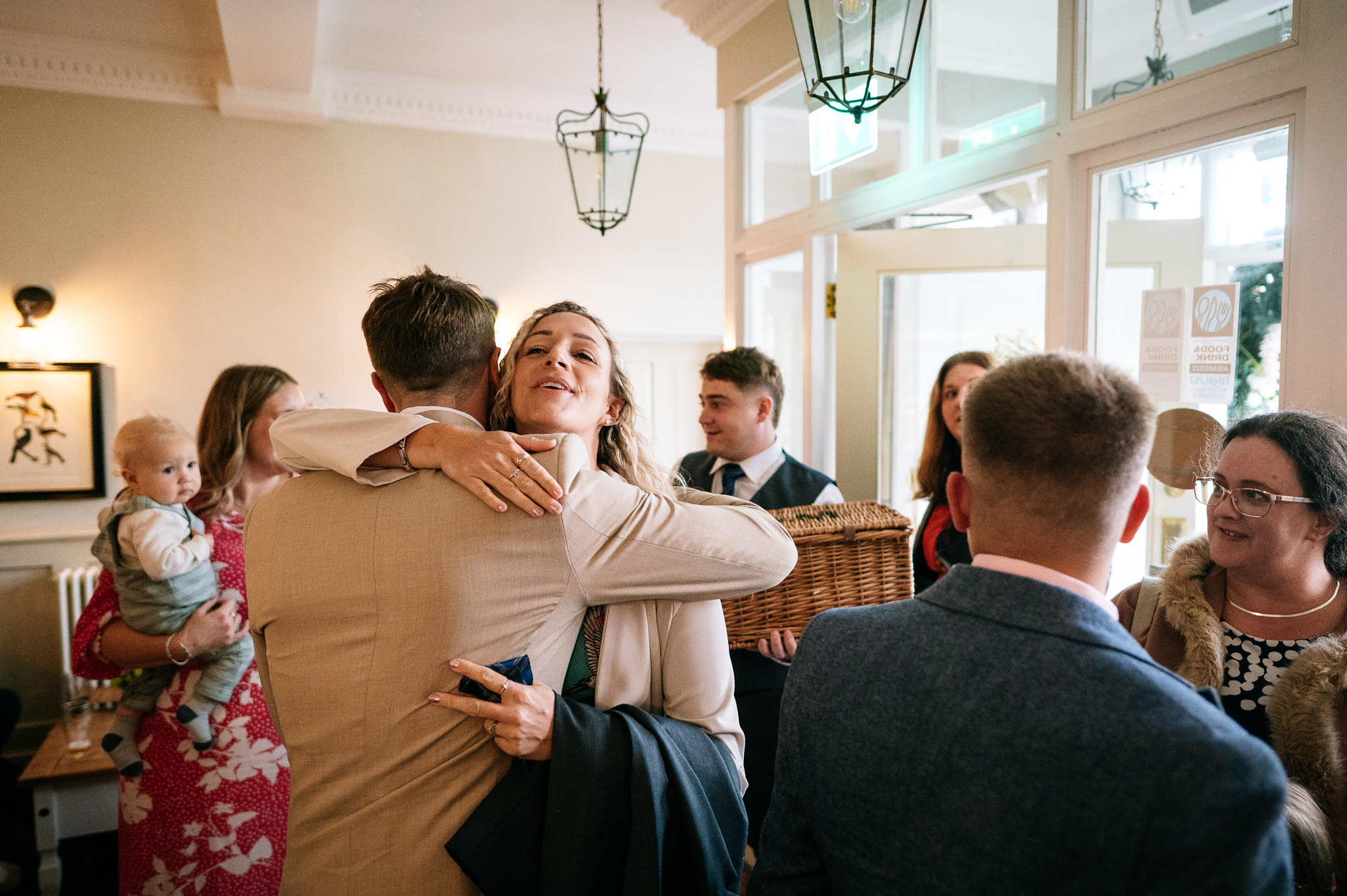 a man in a sand coloured suit with his back to the camera giving a hug to a woman with blonde hair