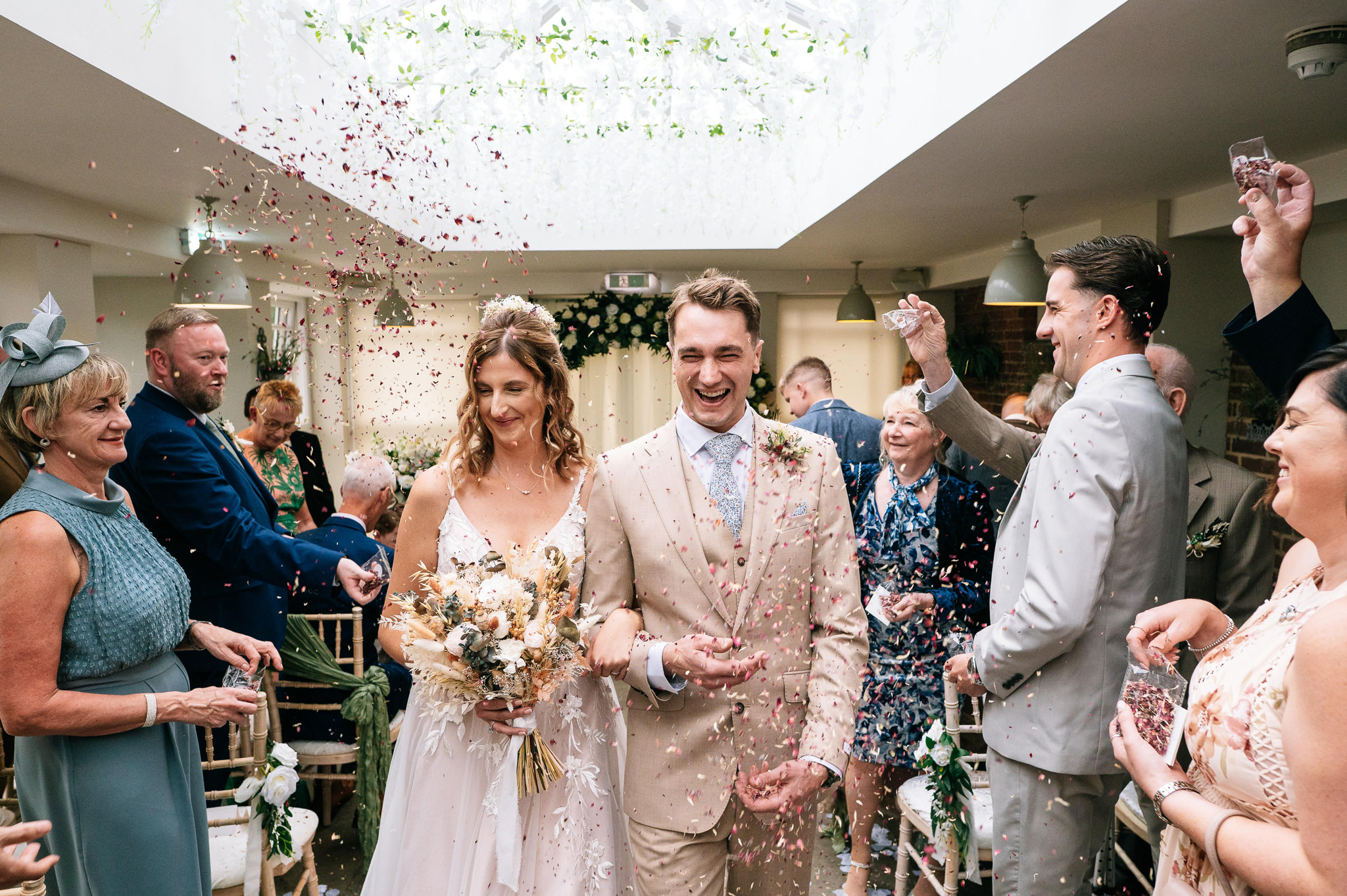 newlyweds walk down the aisle together indoors as their guests shower them with confetti