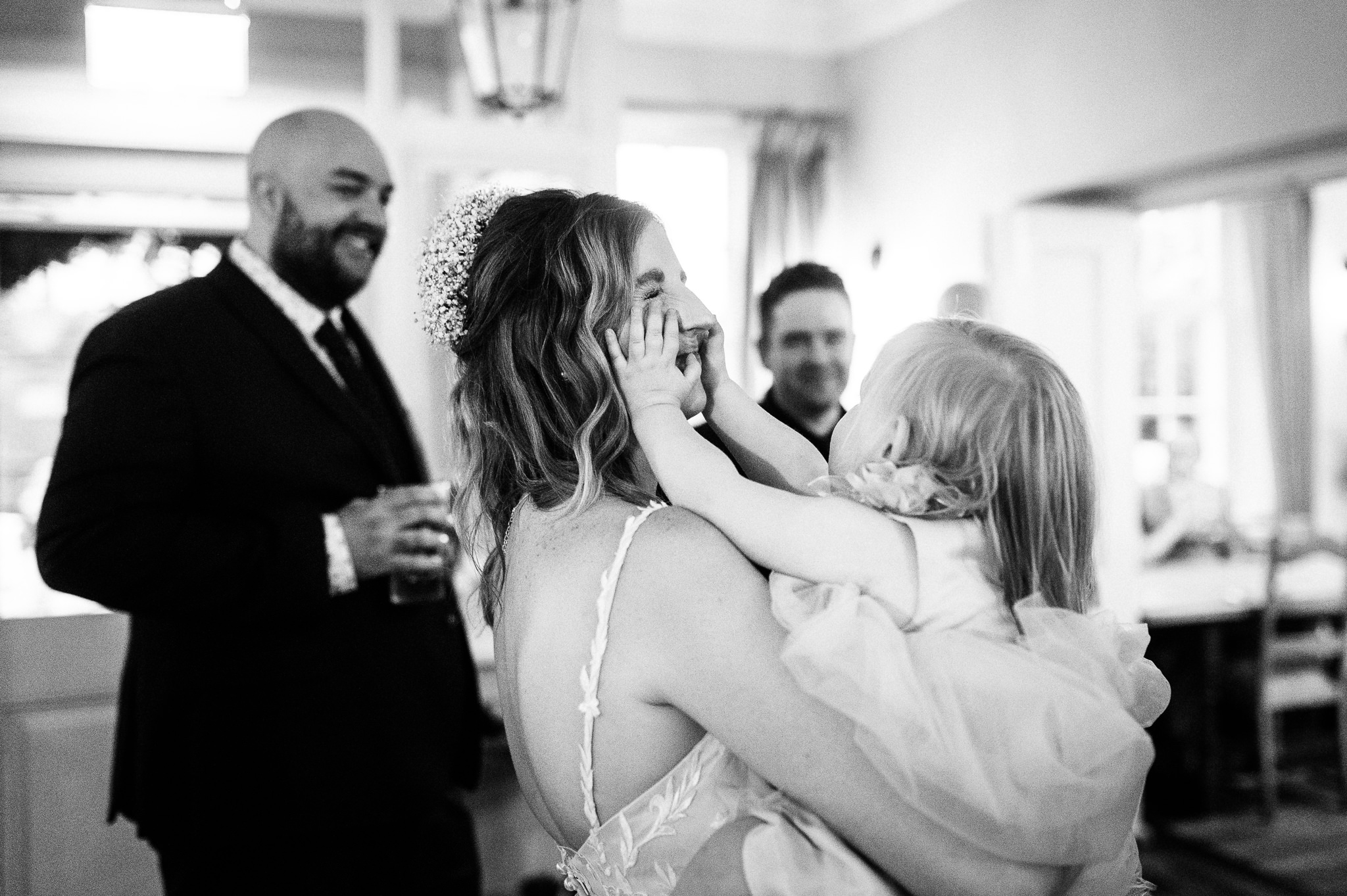 black and white photo of a bride holding her young daughter who's grabbing her mums face
