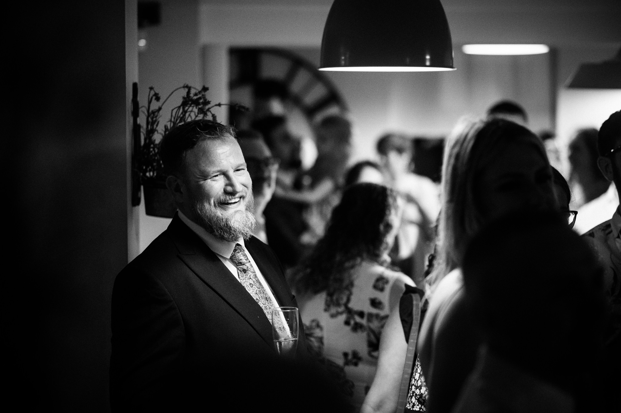 black and white photo of a wedding guest laughing at speeches in a busy room