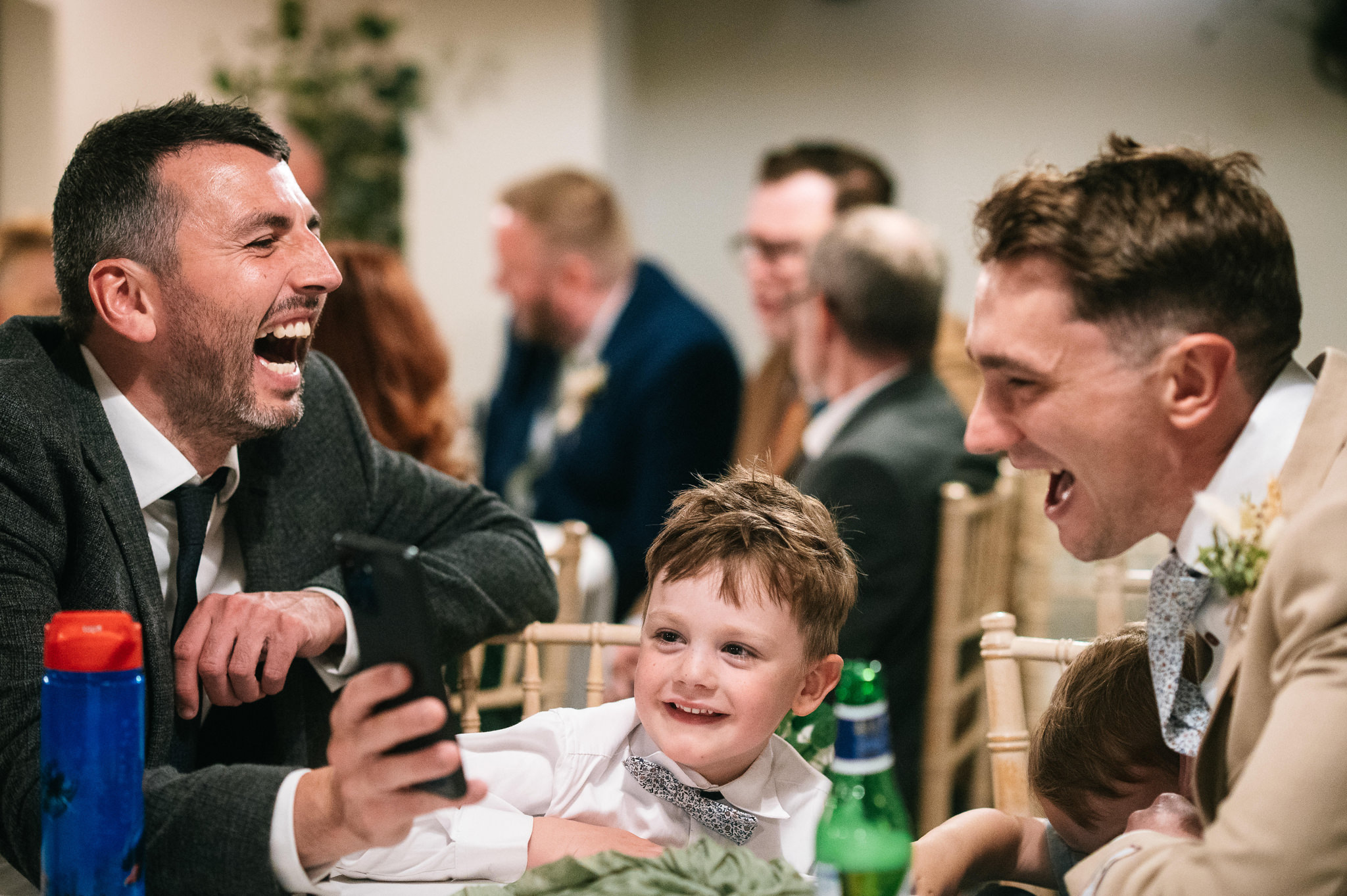 two men in suits and a young boy laughing at something on a phone