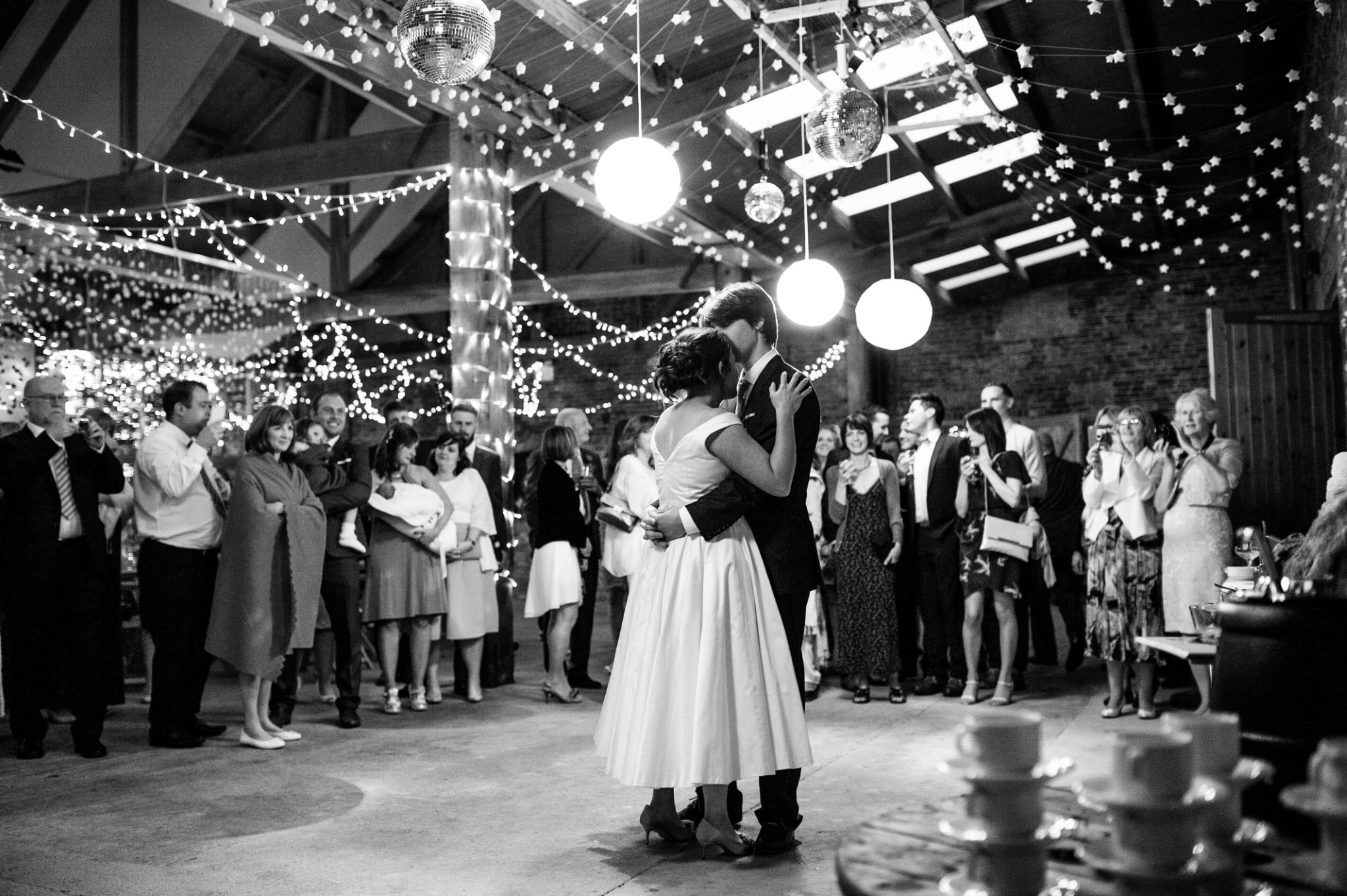 a black and white image of an intimate first dance in a fairy-light lit barn