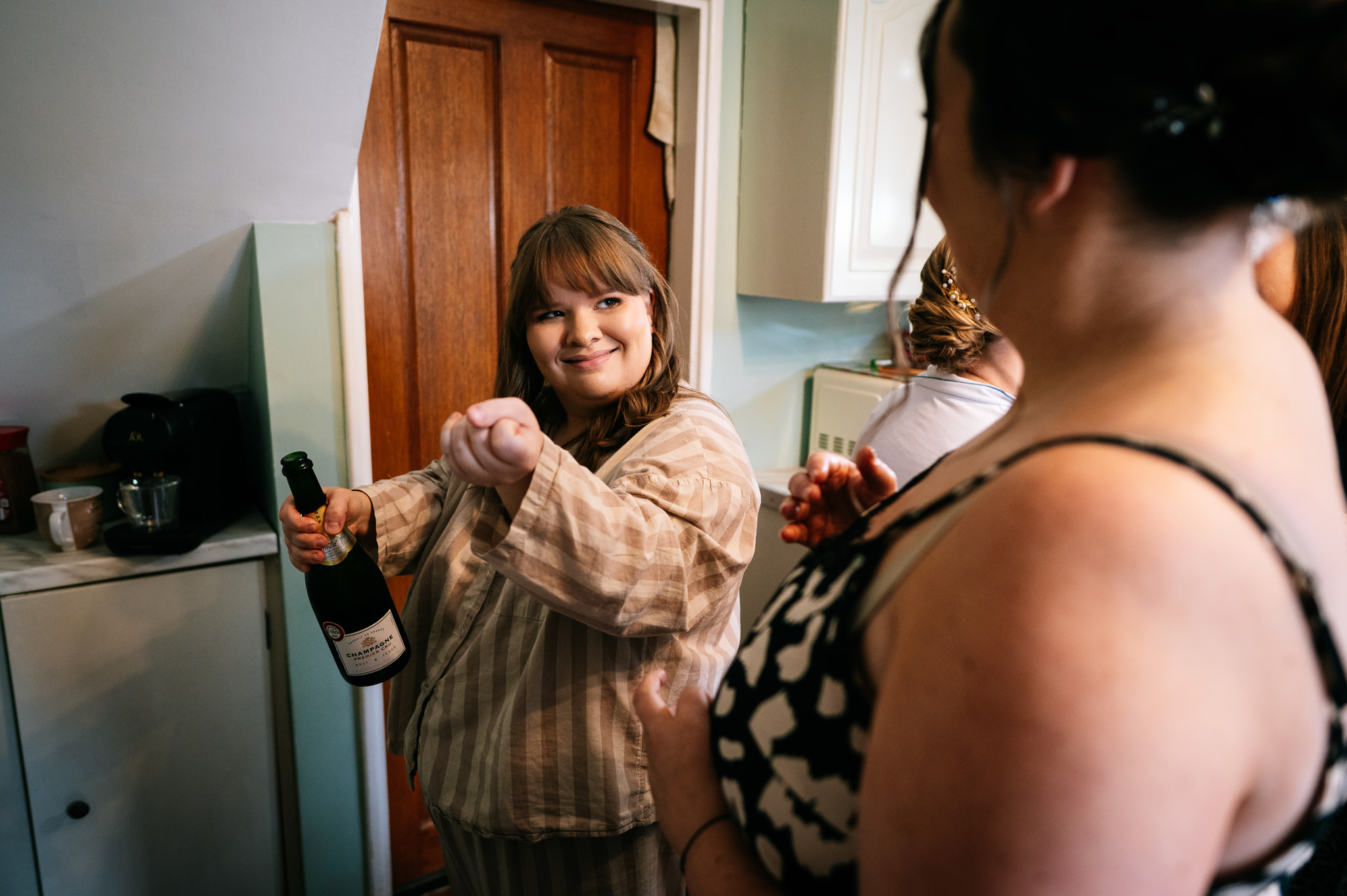 bride's sister pops the top off a bottle of champagne with a smile on her face