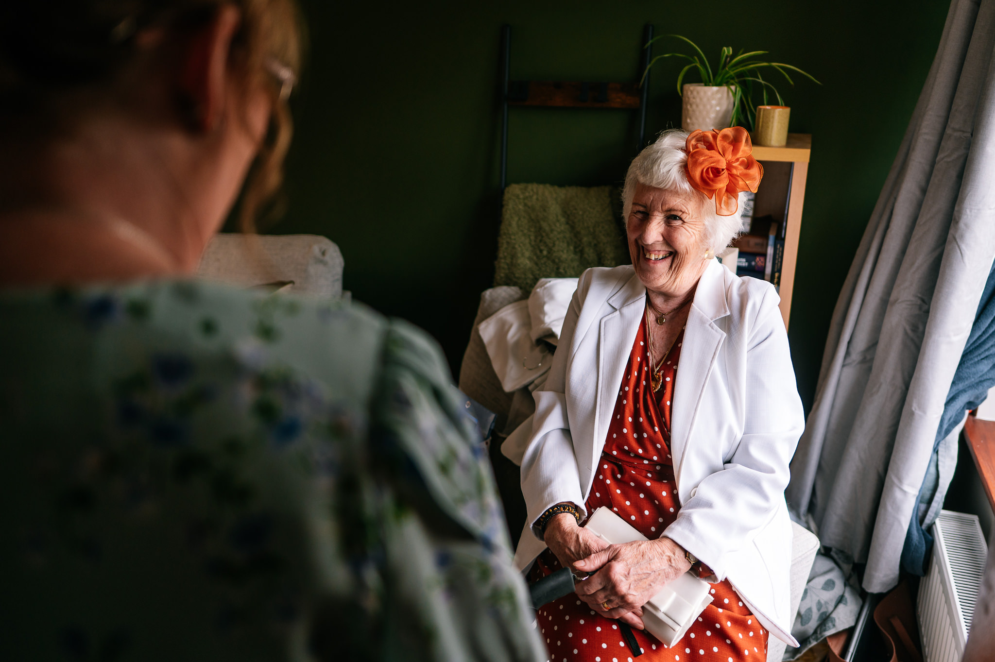 brides grandma sat down smiling wearing a white jacket and a rust coloured dress