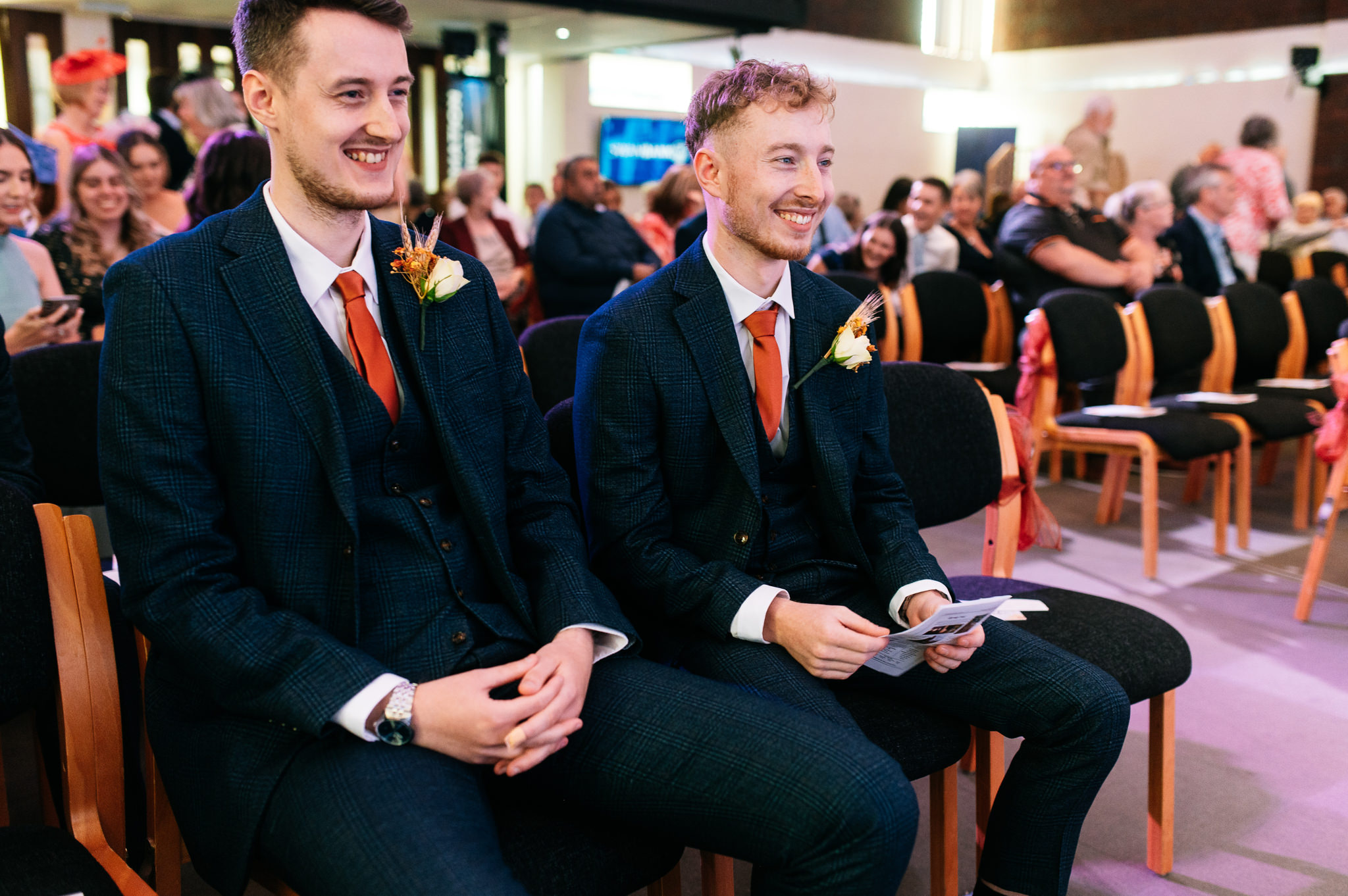 happy smiling groom with a blue suit and orange tie sat down with his best man