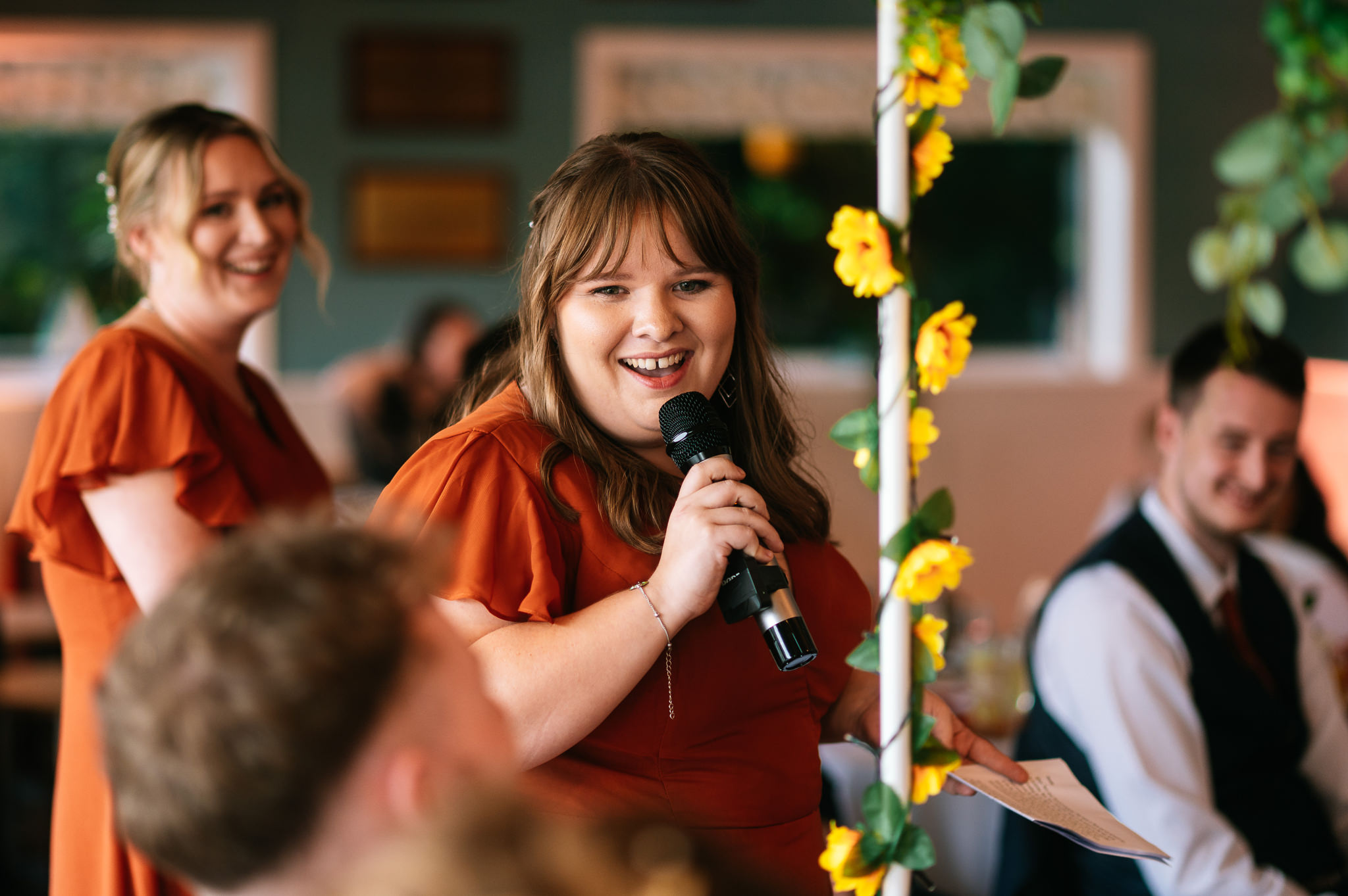 bridesmaid holding a microphone and smiling whilst giving a speech