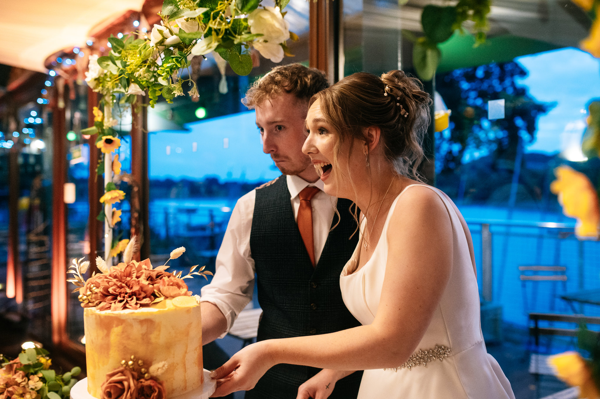 bride and groom pulling funny faces while cutting the wedding cake