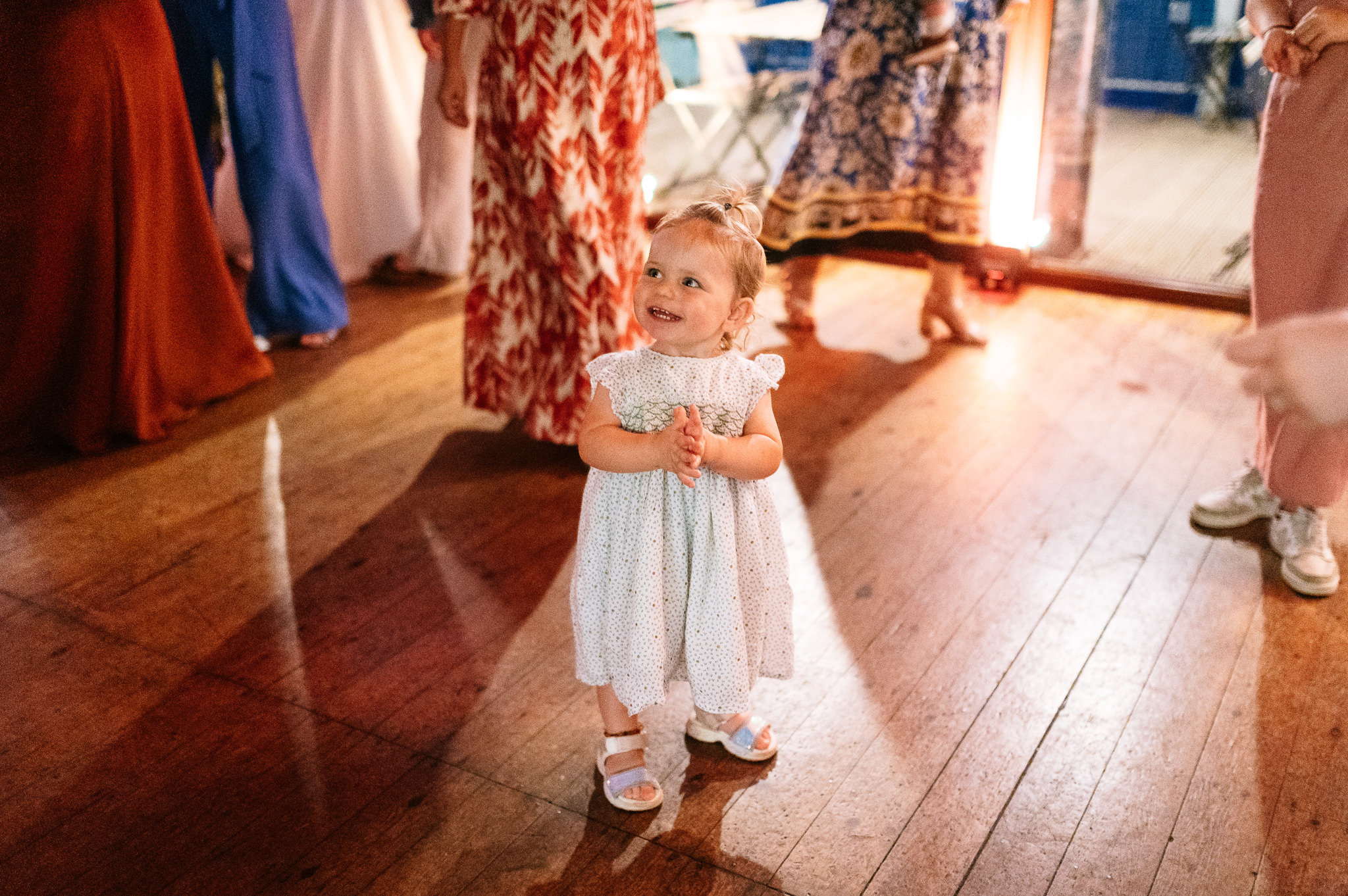 toddler in a white dress smiling and clapping on the dance floor
