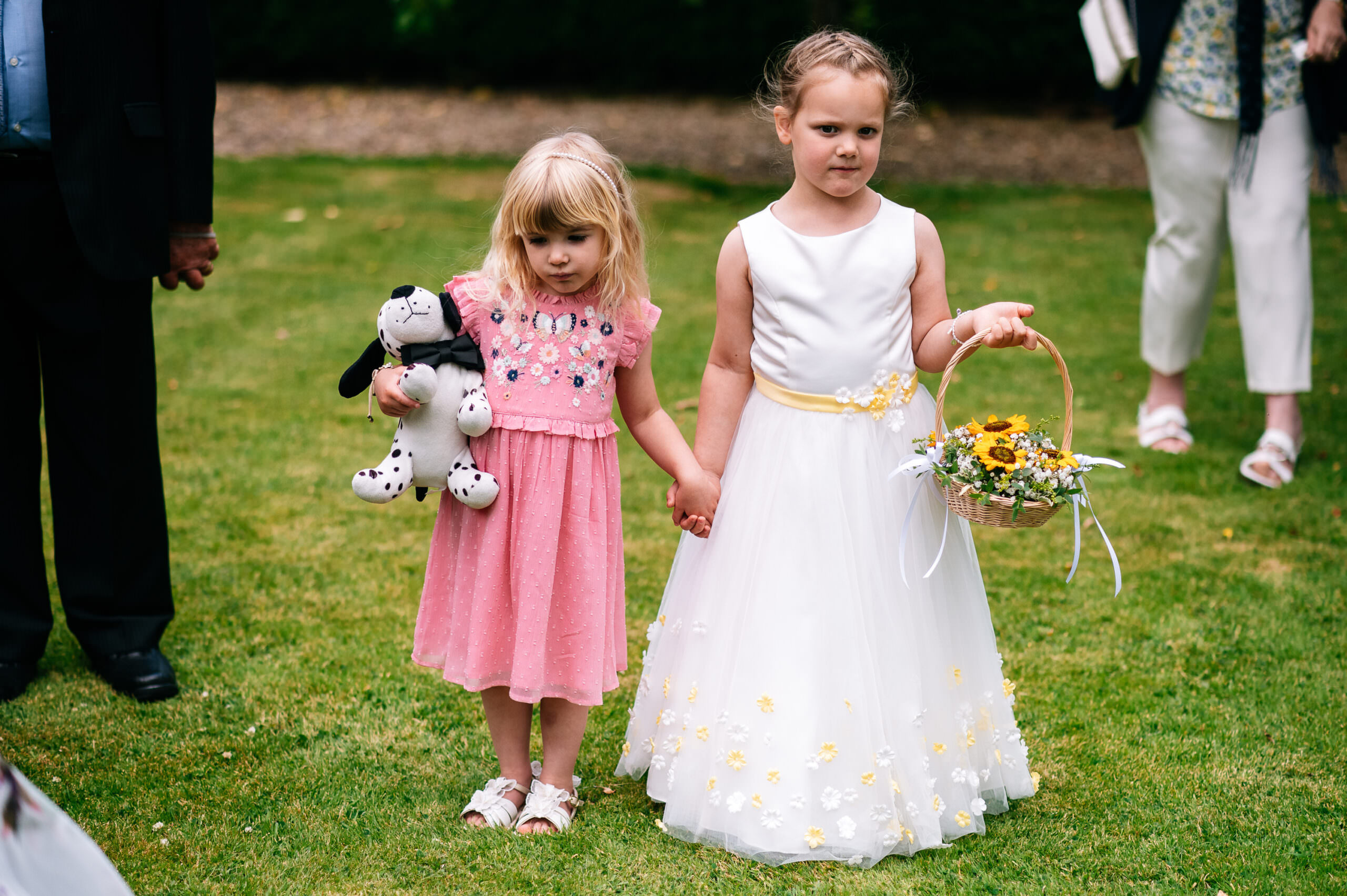 a young flower girl holding hands with a girl in a pink dress both with miserable expressions