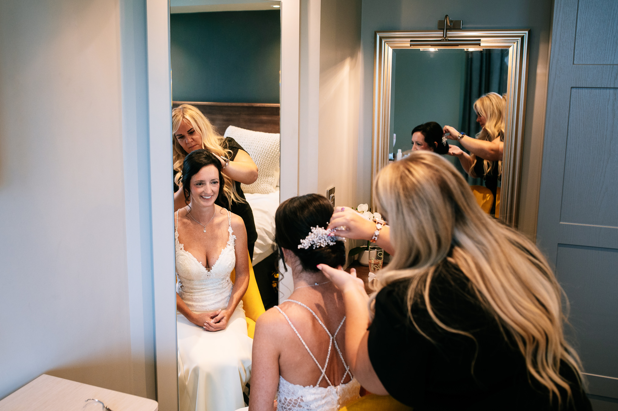 a bride in her wedding dress sat in a hotel room having her hair styled