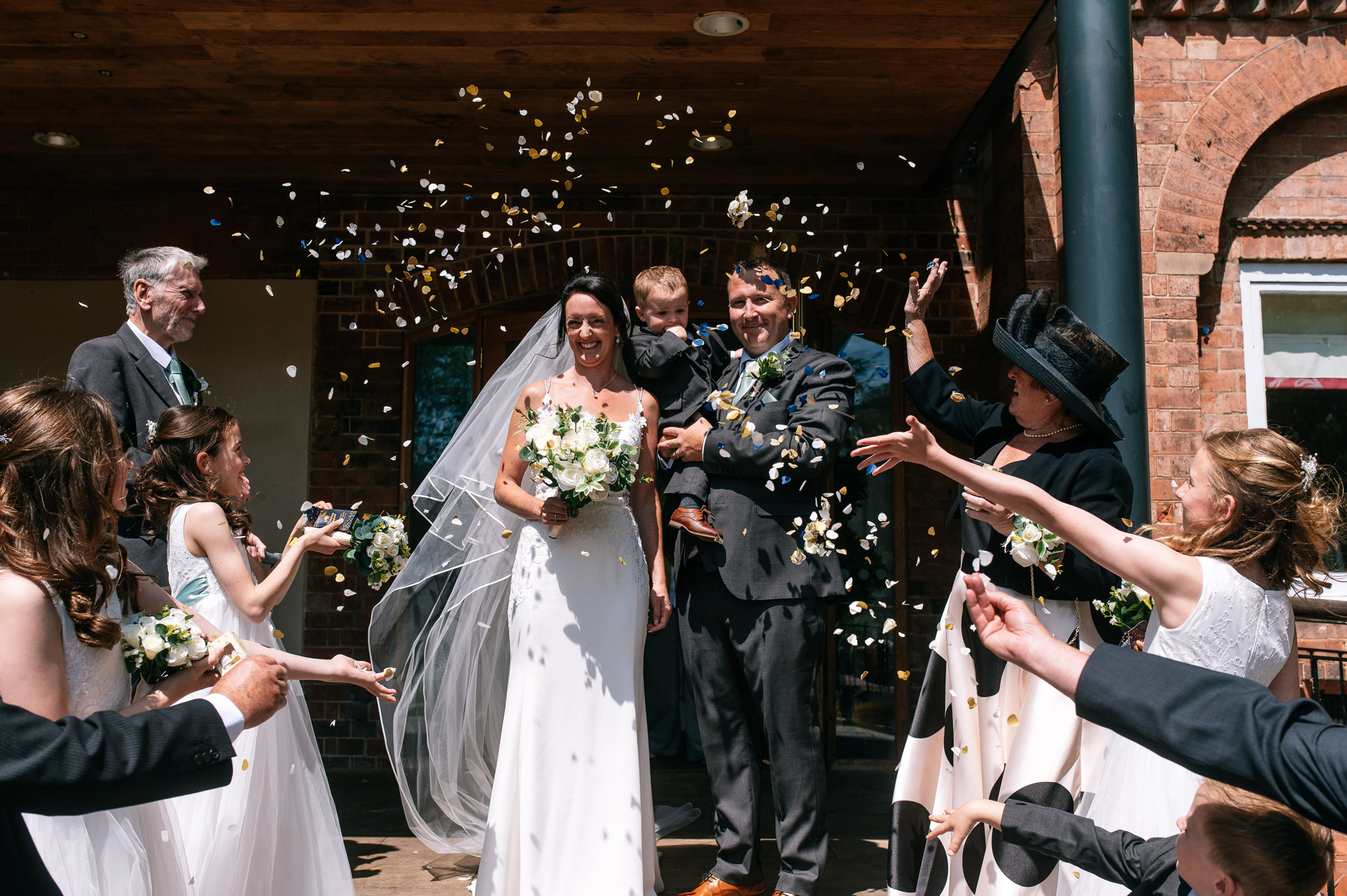 bride and groom holding their young son during the confetti at bridgford hall