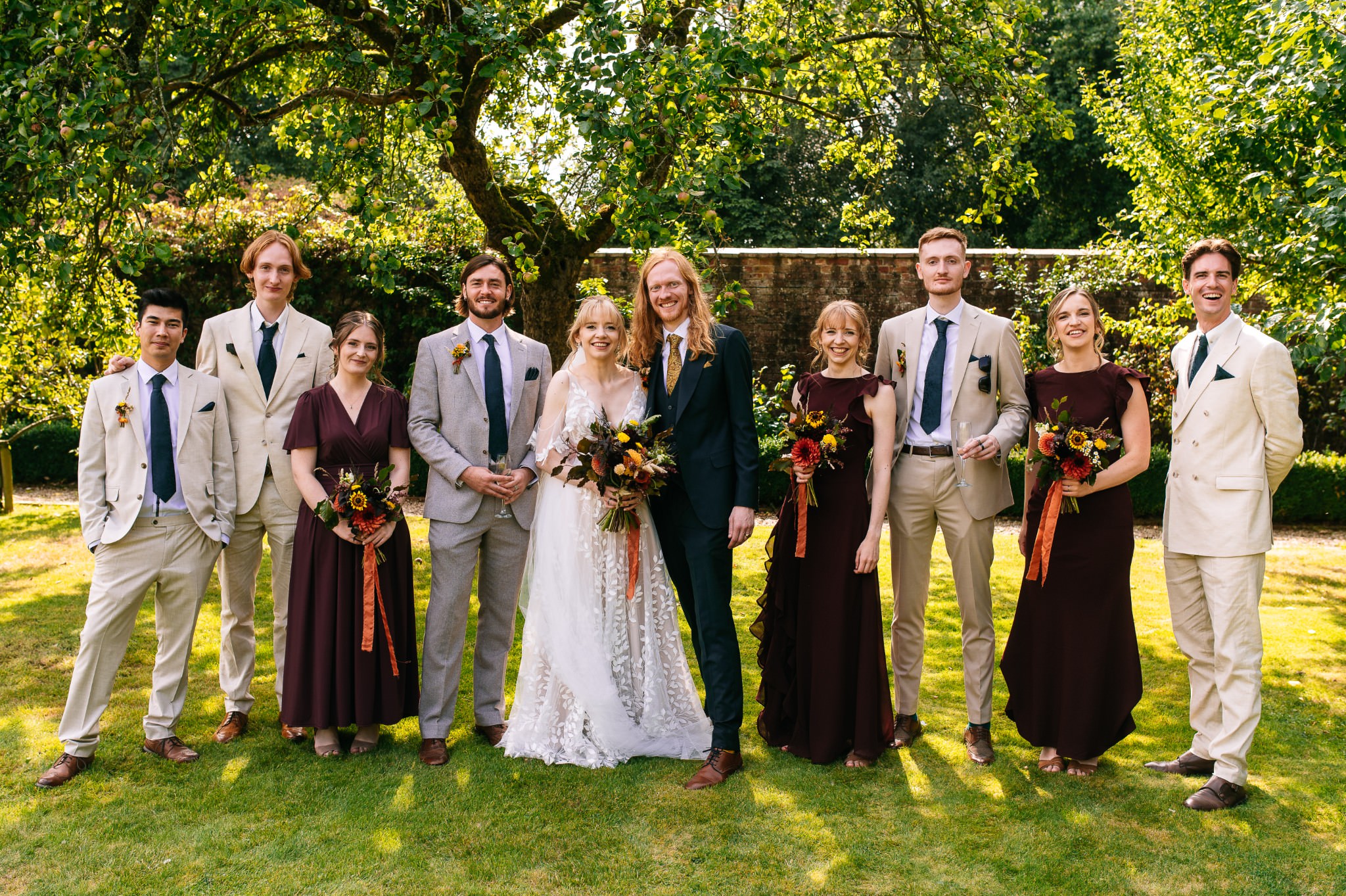 a happy and relaxed group shot of the bride and groom with their bridesmaids and groomsmen taken in a sunny country garden