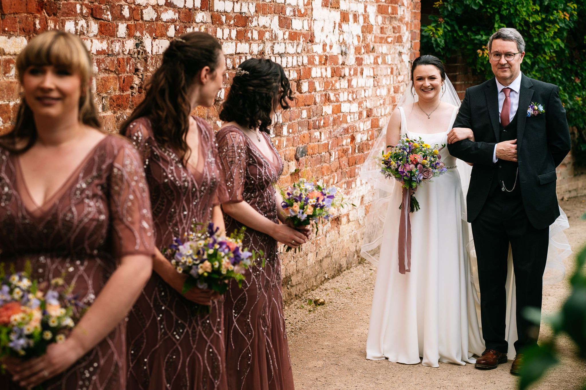 a bride stood with her father while her bridesmaids turn around to look at her