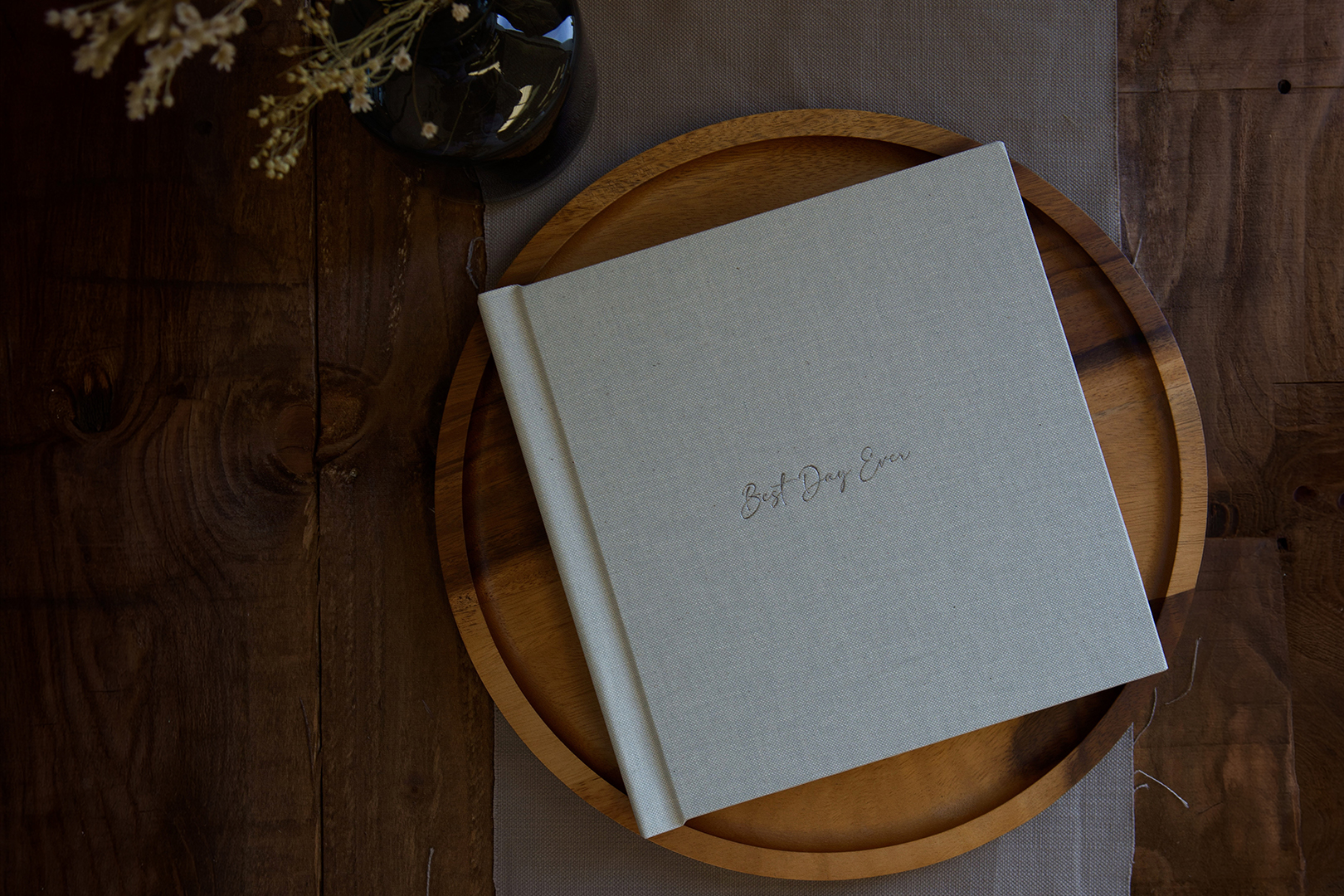 a light grey fabric-covered wedding album sat on a wooden tray against a dark wood table